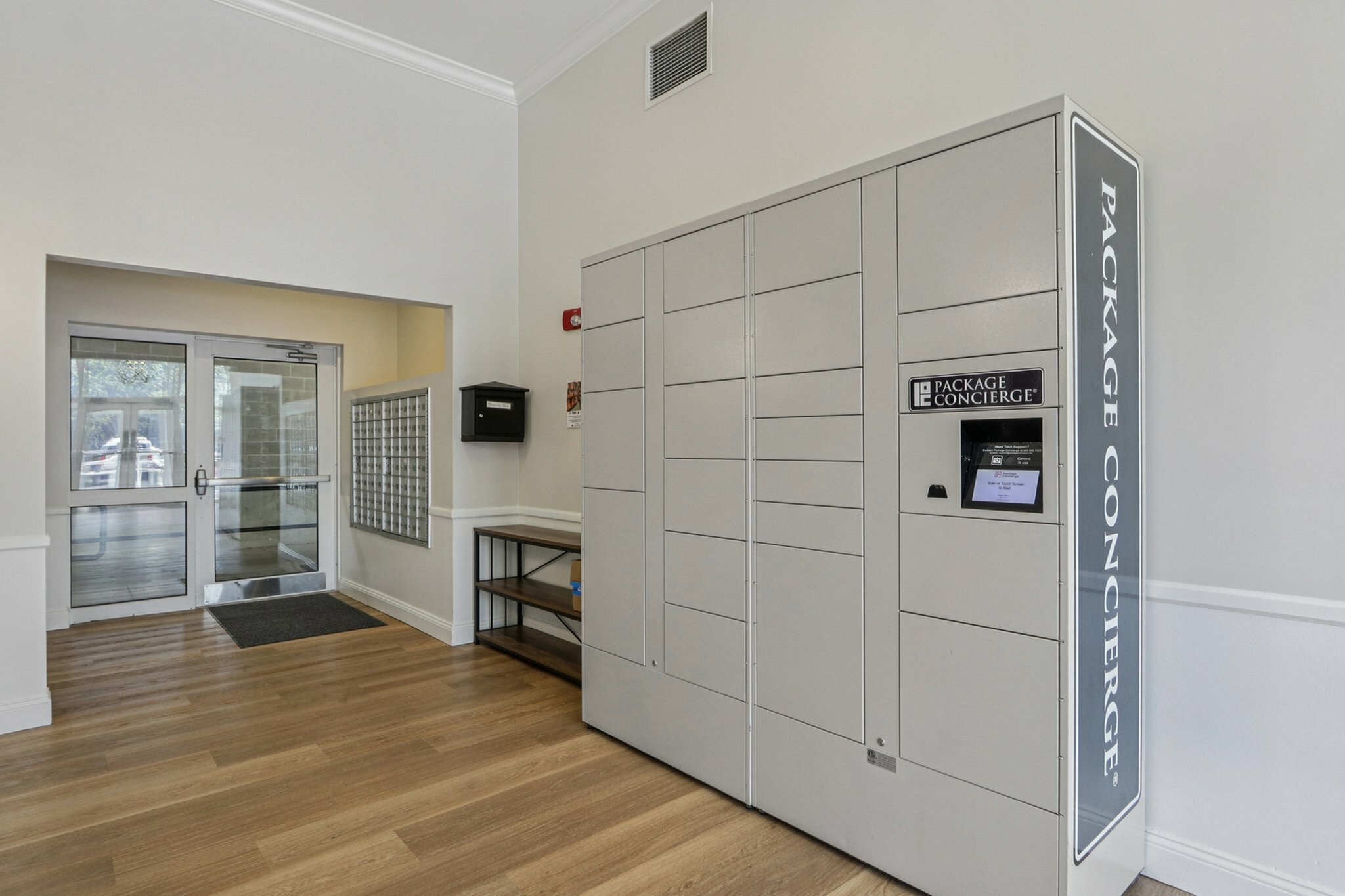 Modern apartment lobby featuring a sleek package concierge system, hardwood floors, and a bright entryway.