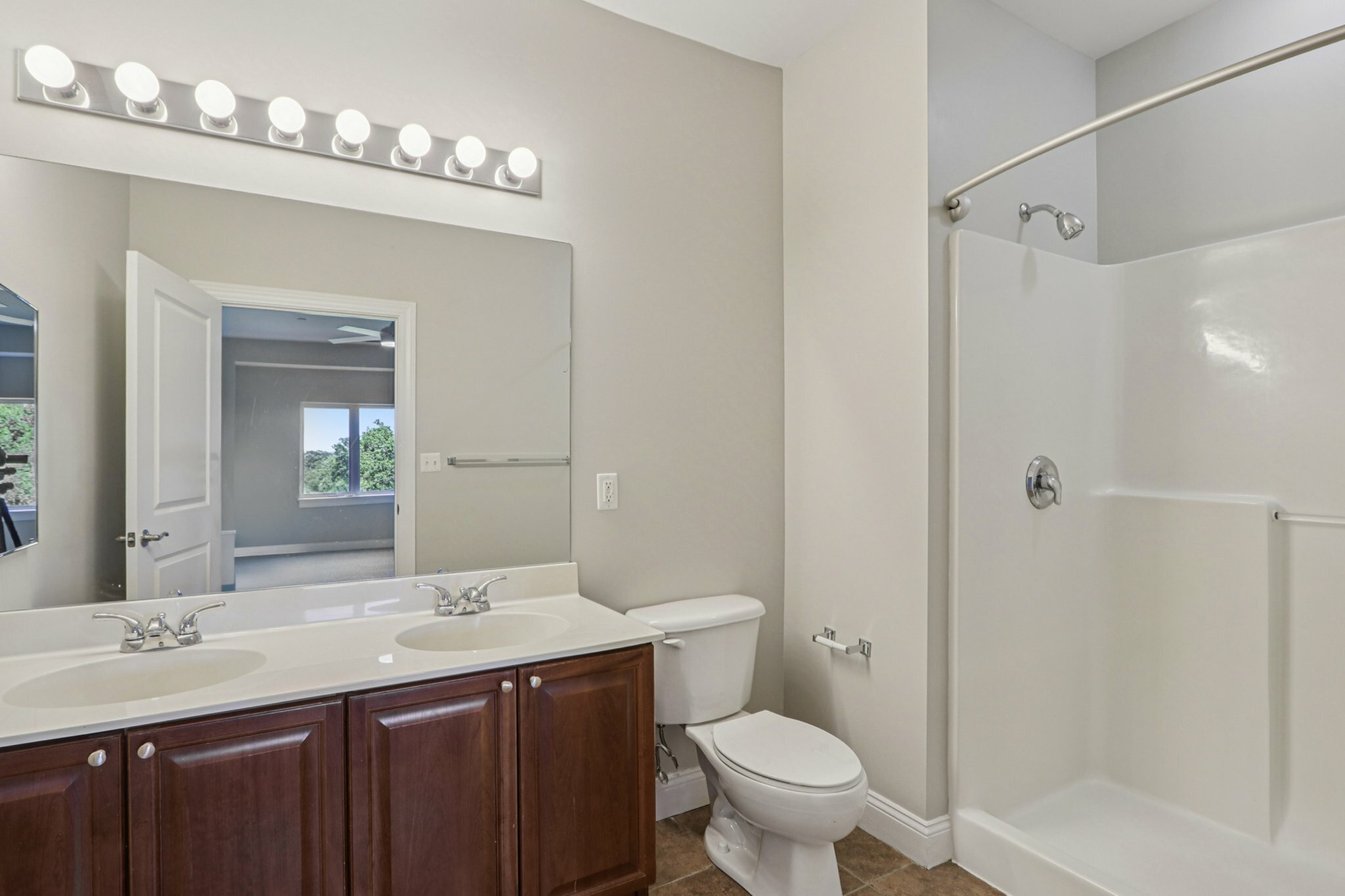 Bright and elegant bathroom with dual sinks and modern fixtures, offering a spacious shower area and stylish vanity lighting.