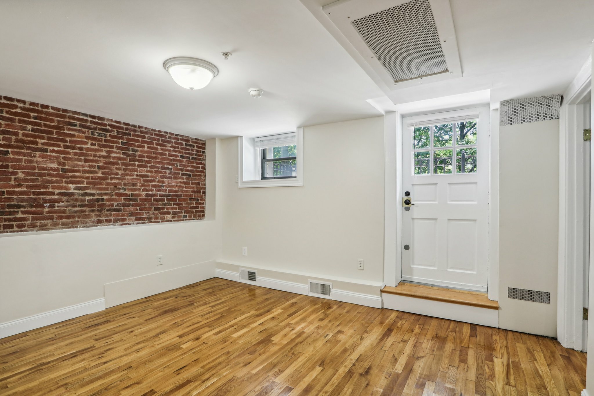 Charming Princeton on Beacon Street studio apartment featuring exposed brick, warm hardwood floors, and a door with natural light from an exterior window.