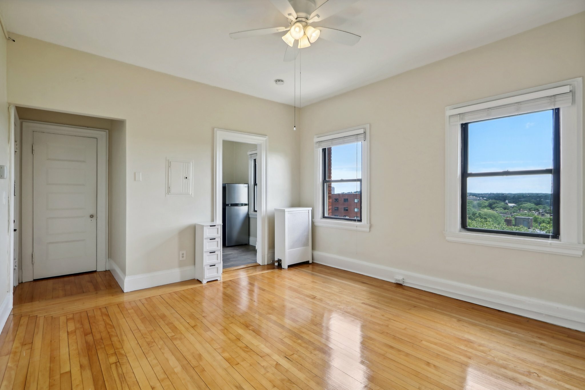 Bright and airy room with polished hardwood floors, large windows offering scenic views, and a modern ceiling fan.