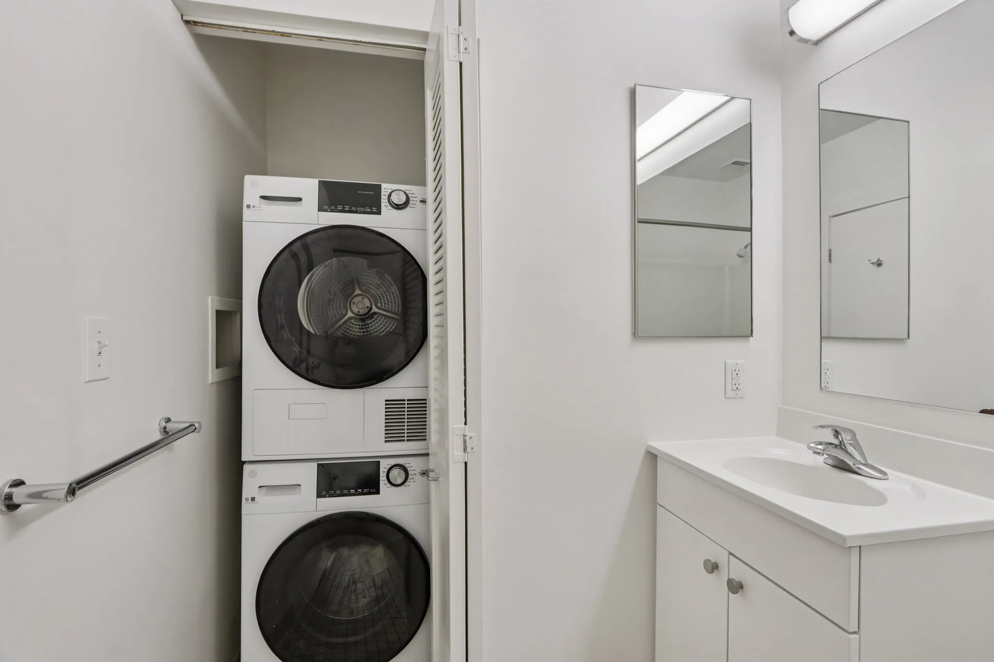 Modern apartment bathroom with sleek stacked washer and dryer, elegant vanity, and contemporary mirror.