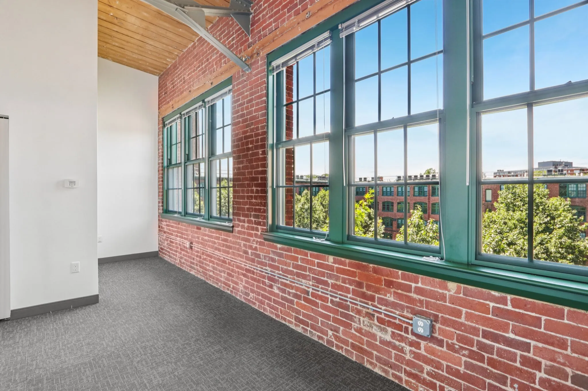 Charming urban loft with exposed brick walls, large windows offering a scenic view, and abundant natural light.