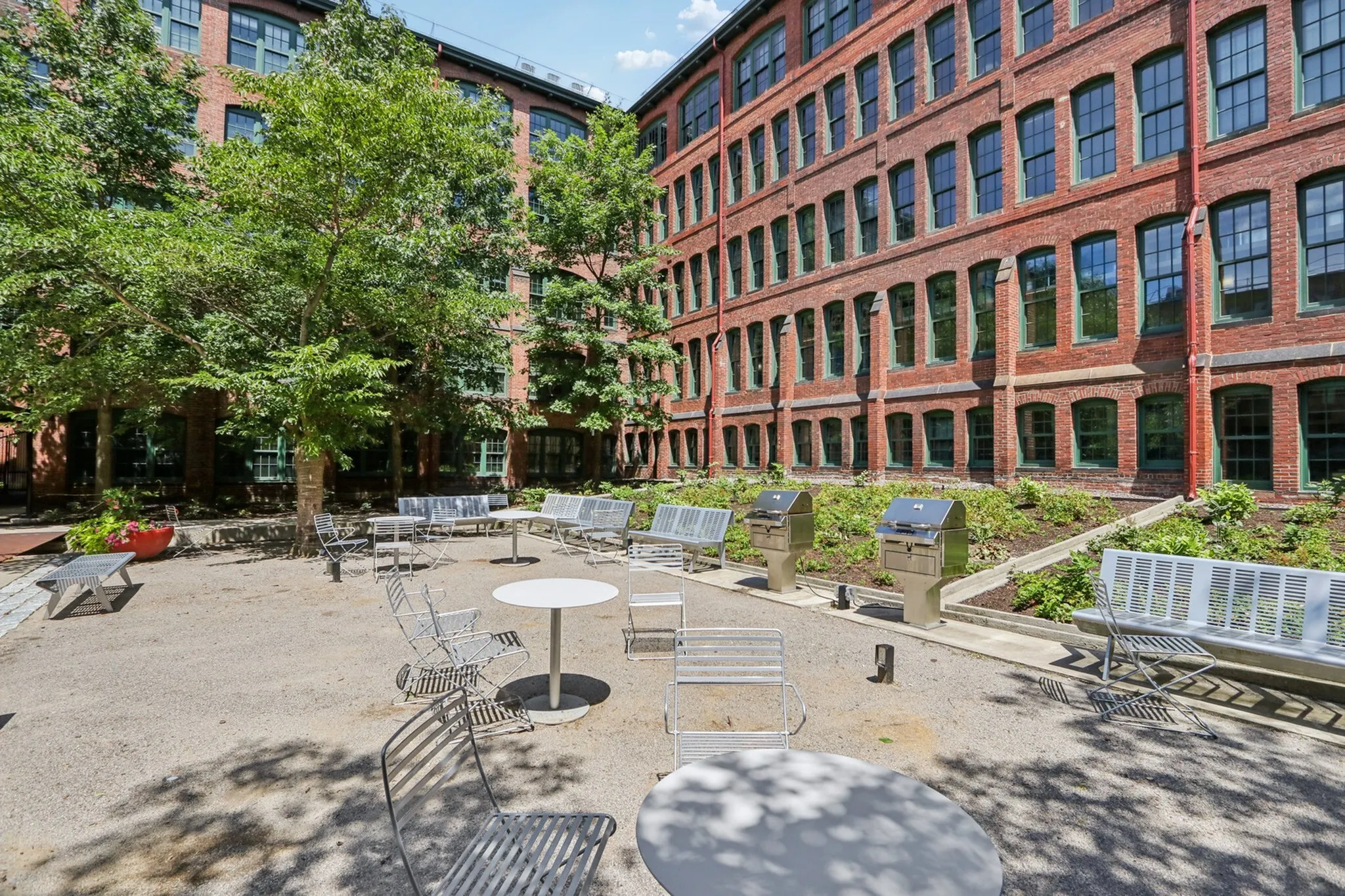 Charming outdoor courtyard with modern seating and BBQ grills, surrounded by a historic brick building and lush greenery.