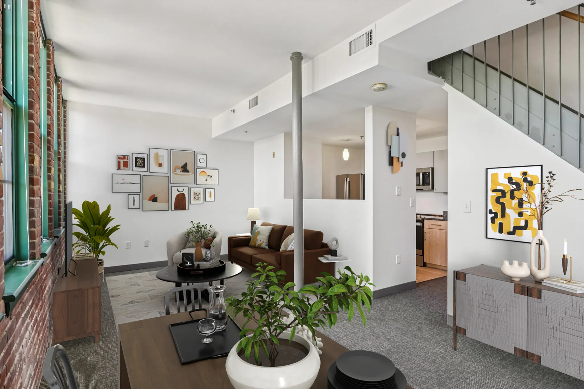 Chic urban living room with exposed brick, large windows, and modern art adorning the walls, featuring a cozy sofa and open connection to a contemporary kitchen.