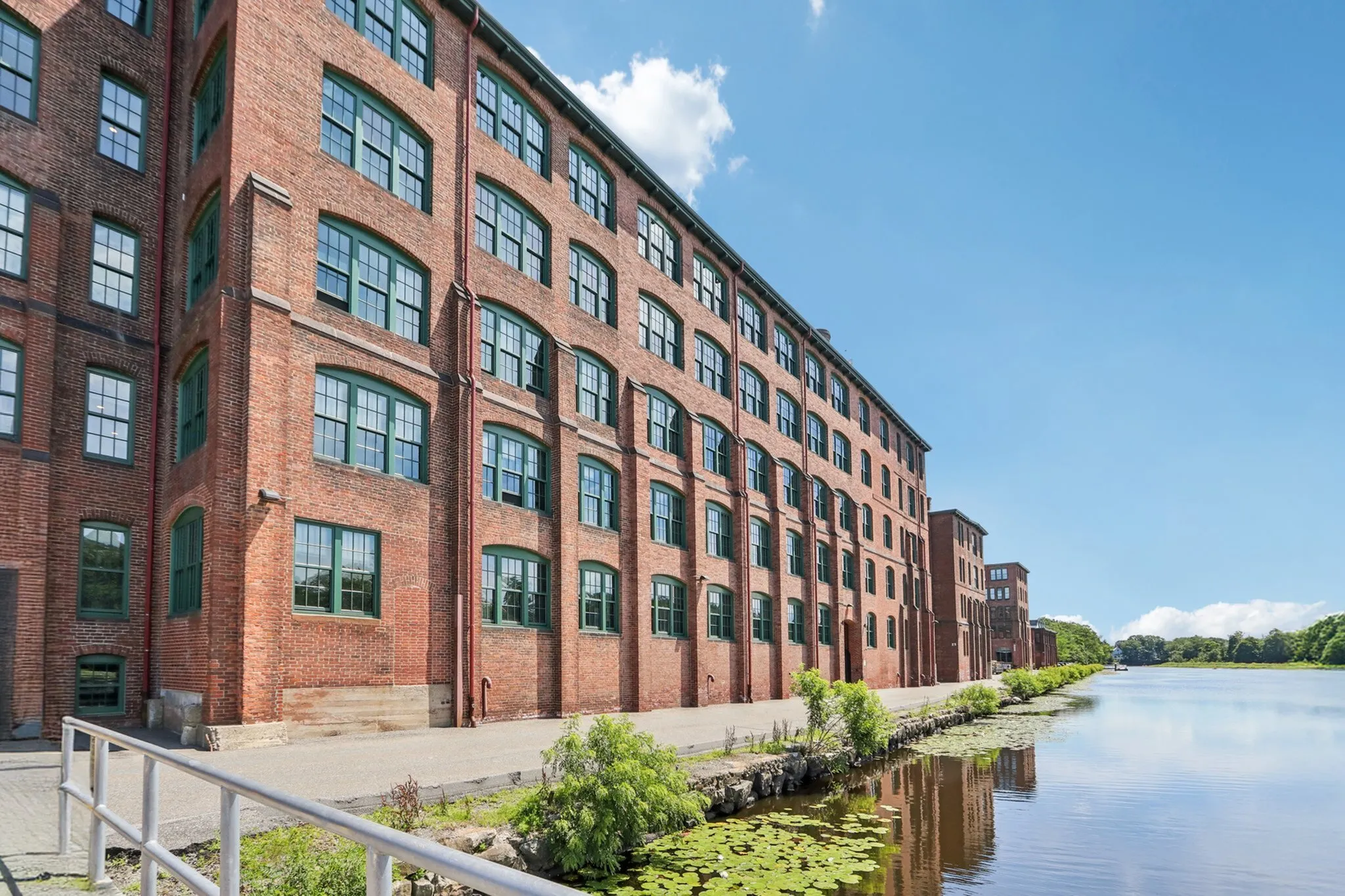 Historic brick apartment building overlooking a serene waterfront with clear blue skies.