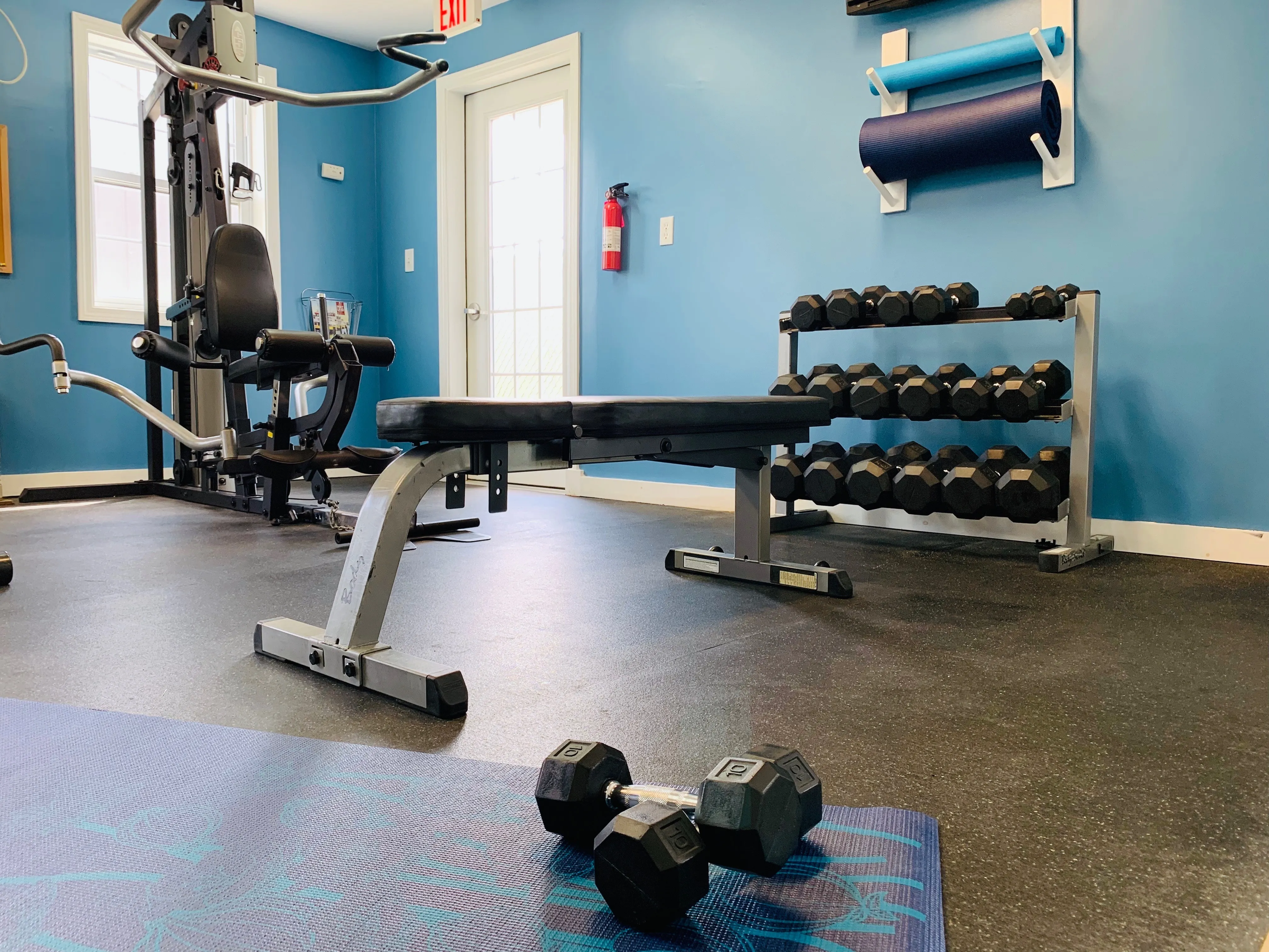 Modern fitness center with a variety of equipment, including weights, a bench, and a multi-functional exercise machine, set in a bright, blue-walled space.