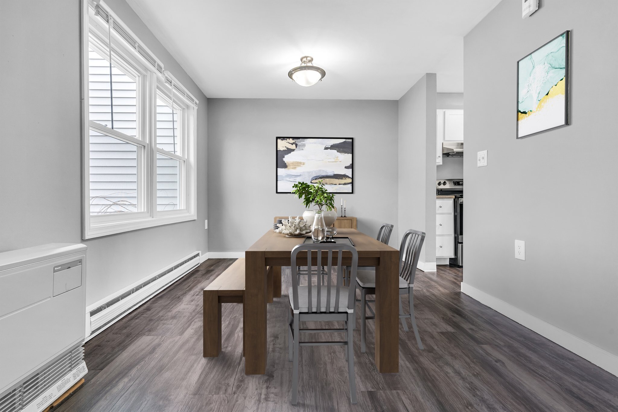 Bright dining area with chic wooden table and modern metal chairs, accented by contemporary artwork and natural light from large windows.