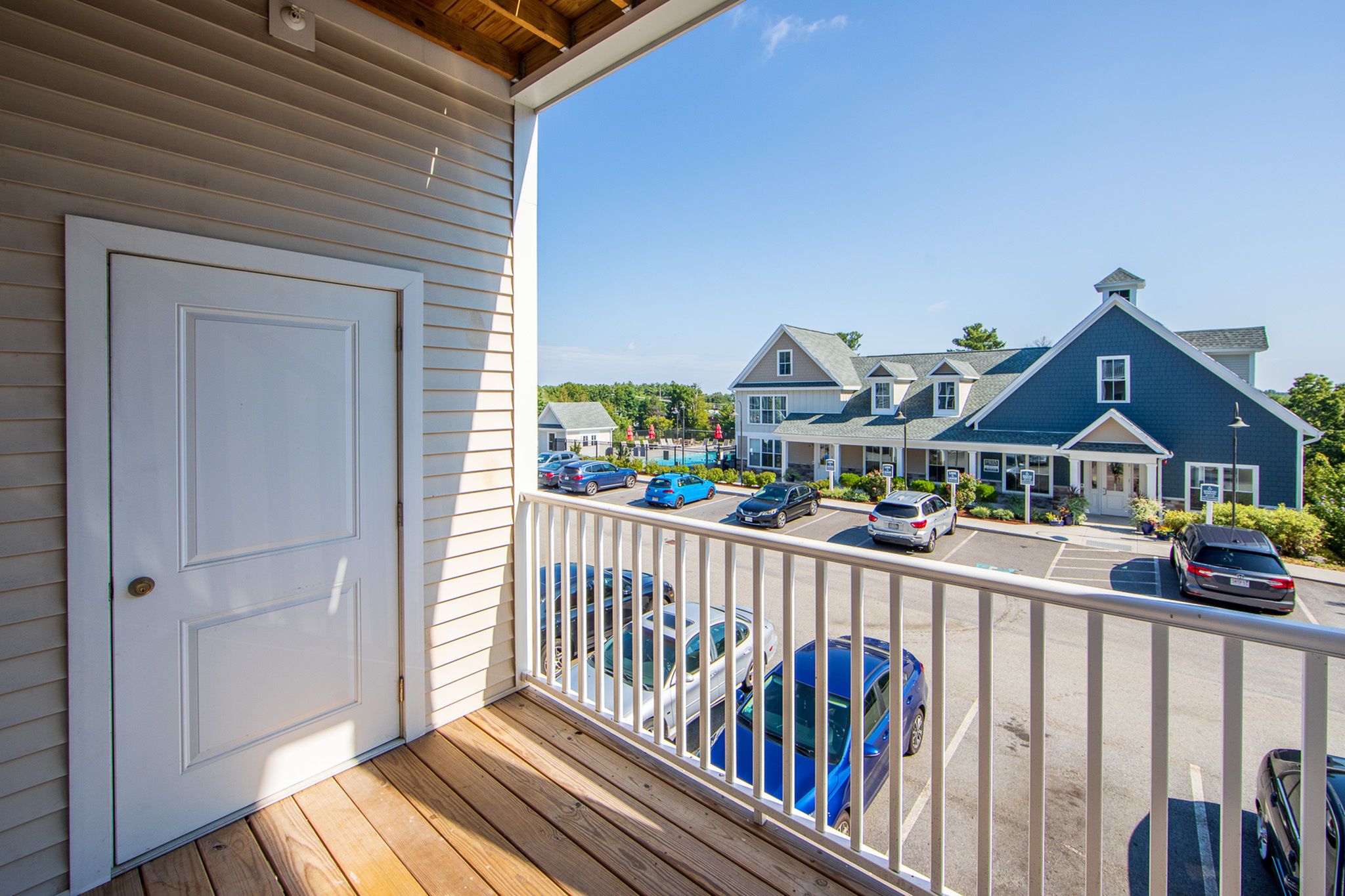 Inviting apartment balcony with a scenic view of charming suburban residences and a vibrant parking area under a clear blue sky.