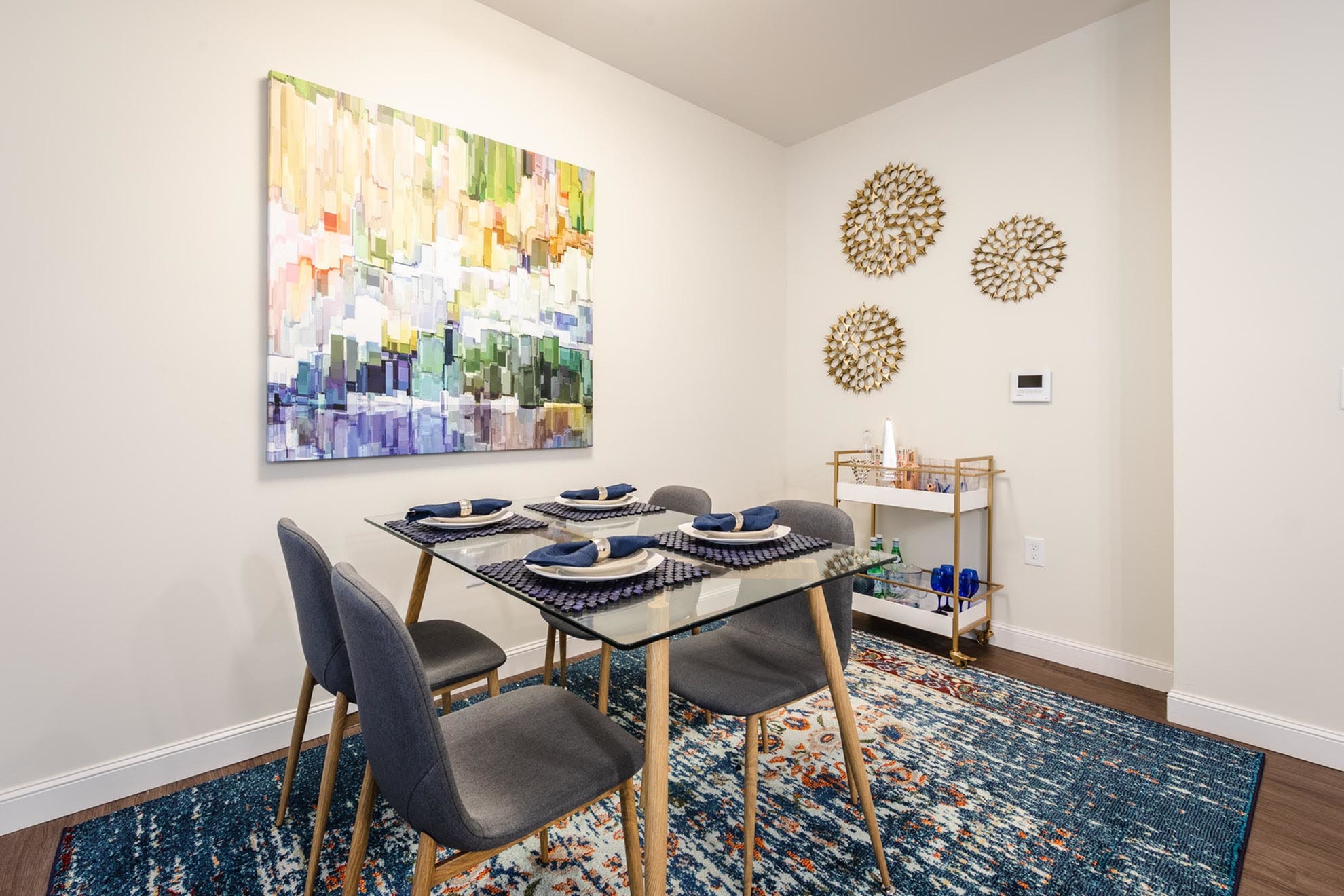 Contemporary dining area with elegant glass table, vibrant abstract artwork, and chic wall decor, offering a stylish and inviting atmosphere.