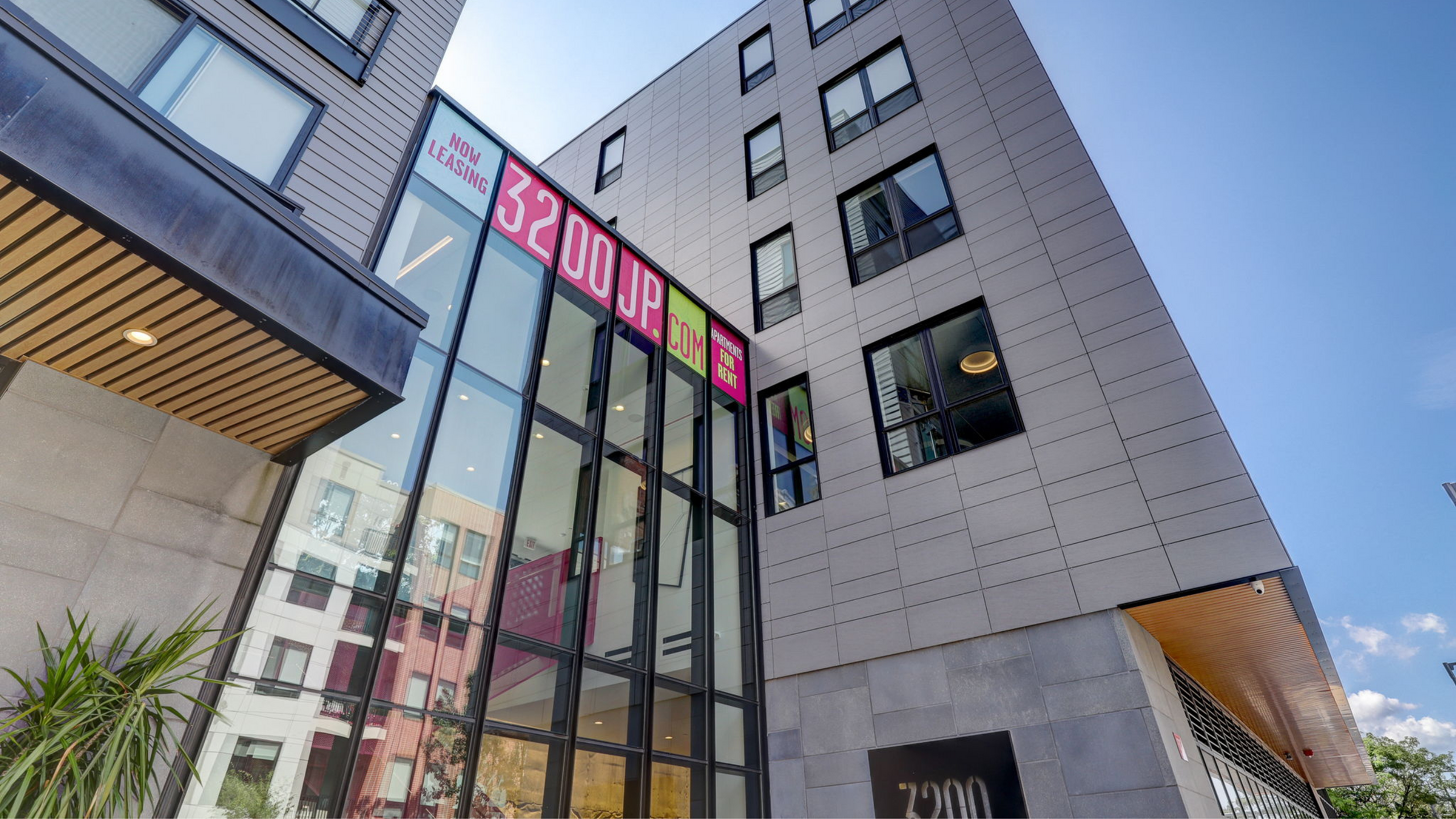 3200 Washington Apartments | Contemporary apartment building with sleek glass facade and rental signage under a clear blue sky. | Apartments for Rent boston ma