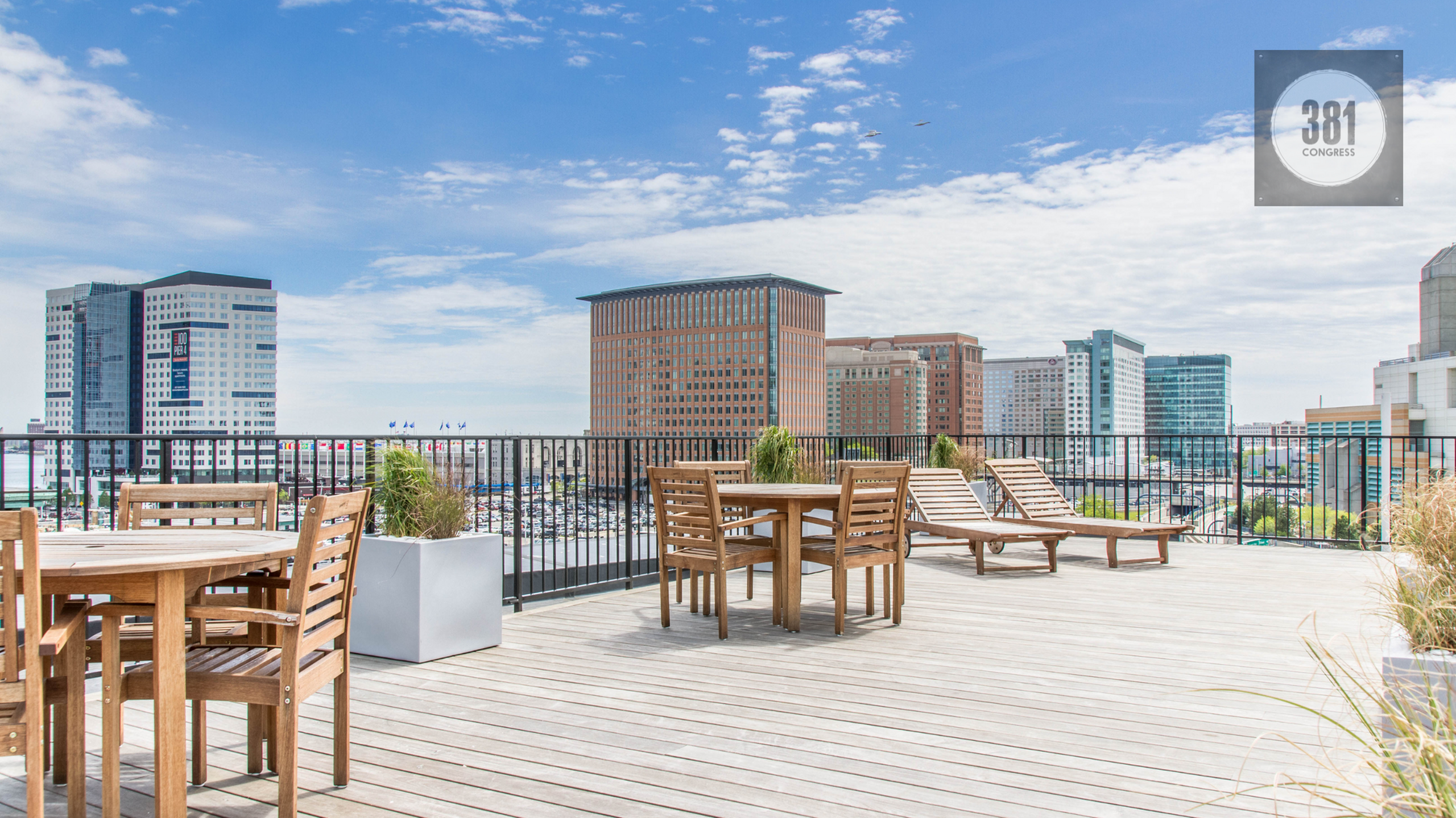 381 Congress Lofts | Stylish rooftop terrace with wooden furniture and a panoramic city skyline view. | Loft Apartments in Boston MA