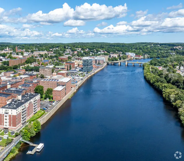 Aerial view of a vibrant riverside cityscape with modern apartment buildings and lush greenery.