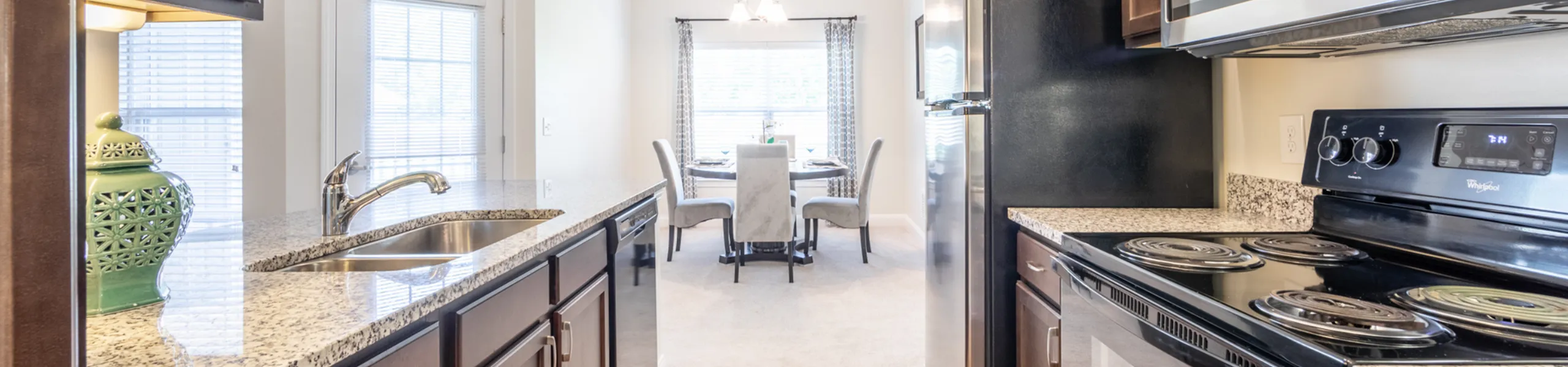 Elegant kitchen with granite countertops, modern stainless steel appliances, and a sunlit dining area in the background.