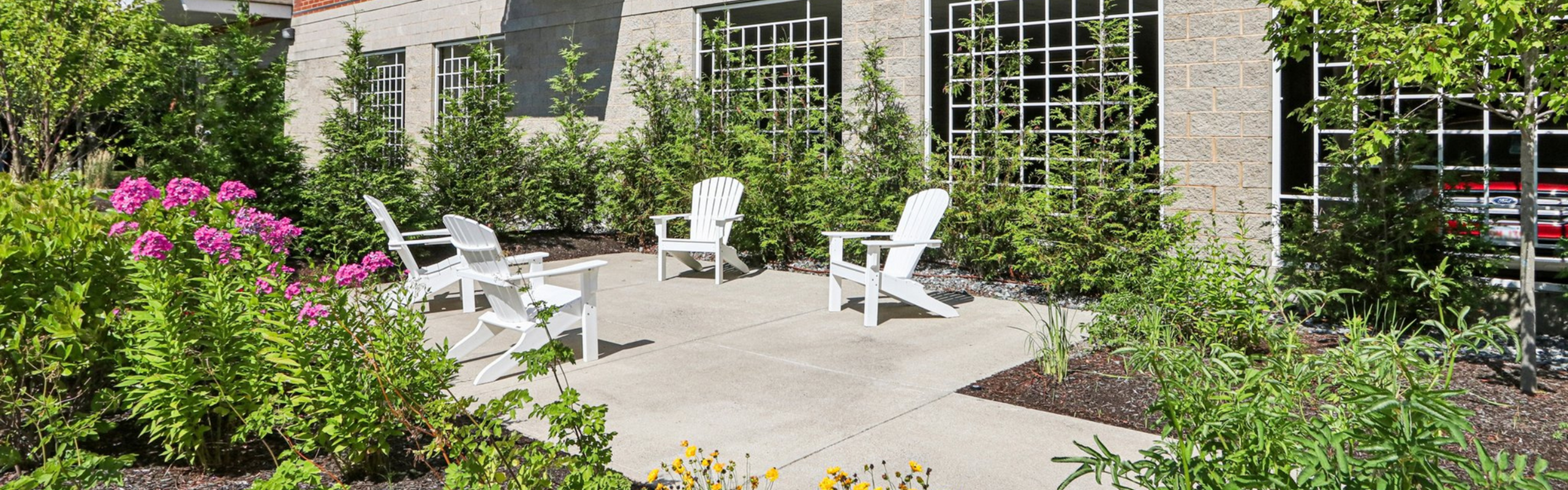 Charming outdoor patio with white Adirondack chairs surrounded by lush greenery and vibrant flowers.