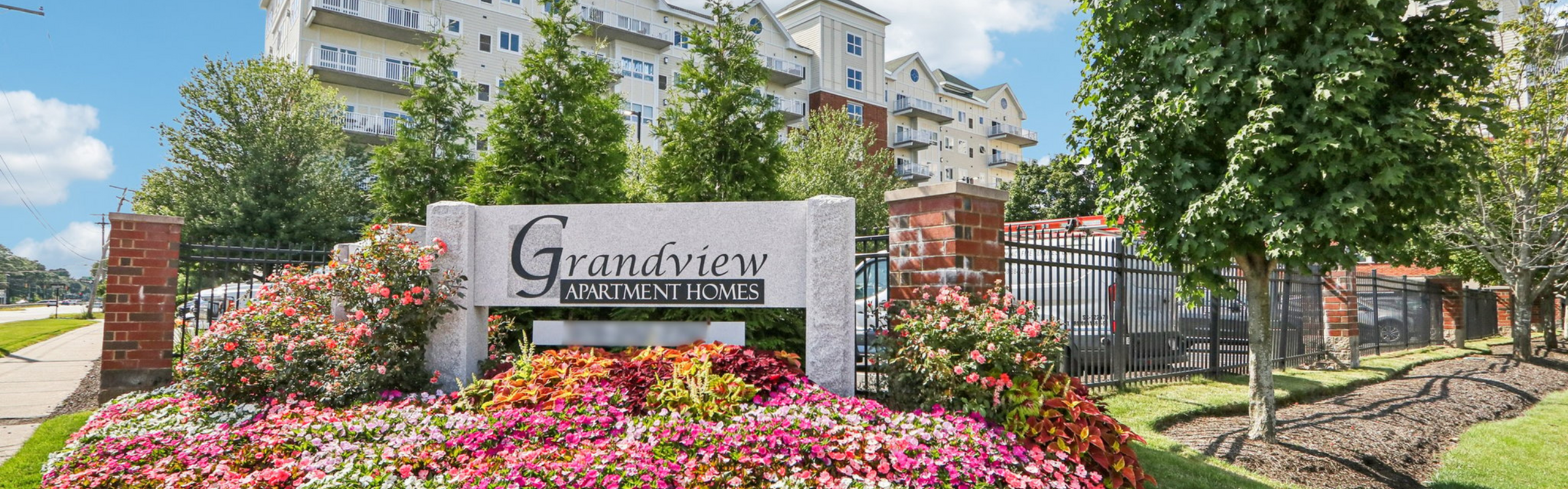 Inviting entrance of Grandview Apartment Homes surrounded by vibrant gardens and lush trees, offering scenic and comfortable living.