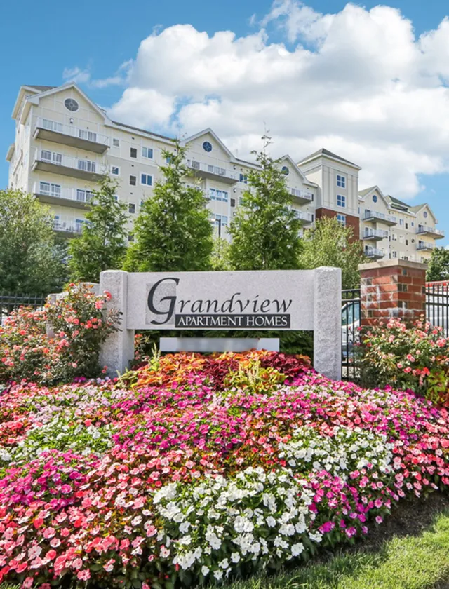 Grandview Apartments | Grandview Apartment Homes showcasing a charming garden with vibrant flowers and a welcoming entrance against a backdrop of a beautiful multi-story building. | Waterfront apartments in lowell ma