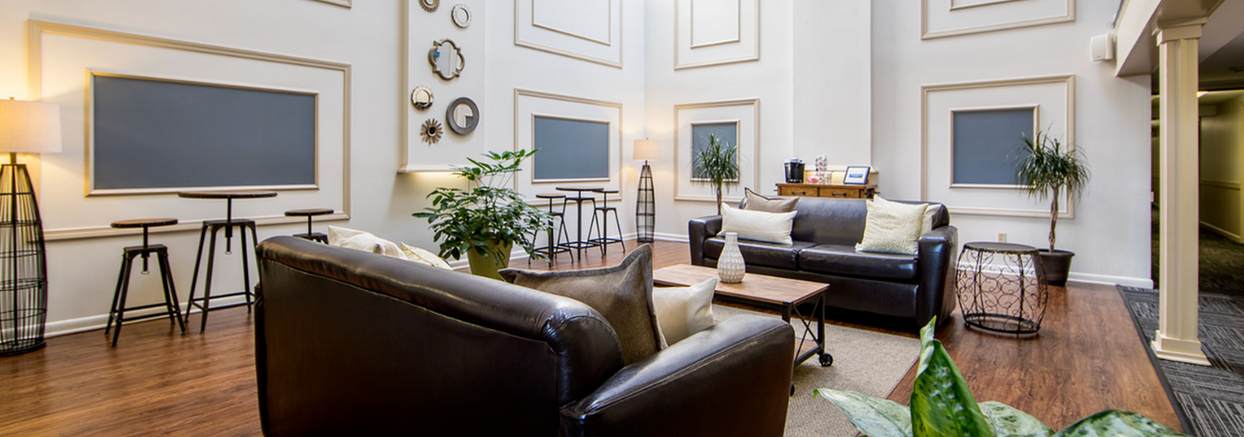 Elegant and inviting lobby with high ceilings featuring cozy leather couches, modern wall decor, and lush greenery, offering a welcoming atmosphere.