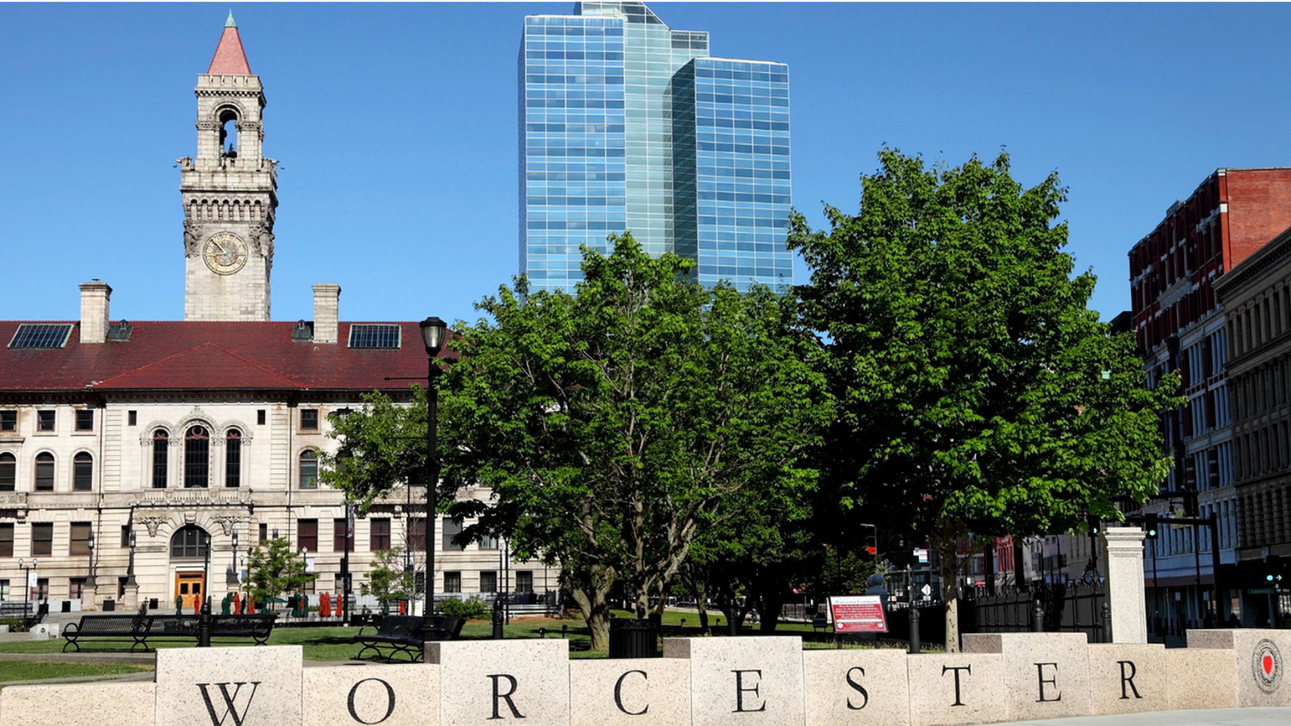 Charming cityscape featuring historic architecture with a prominent clock tower alongside a modern, glass-fronted building against a clear blue sky.
