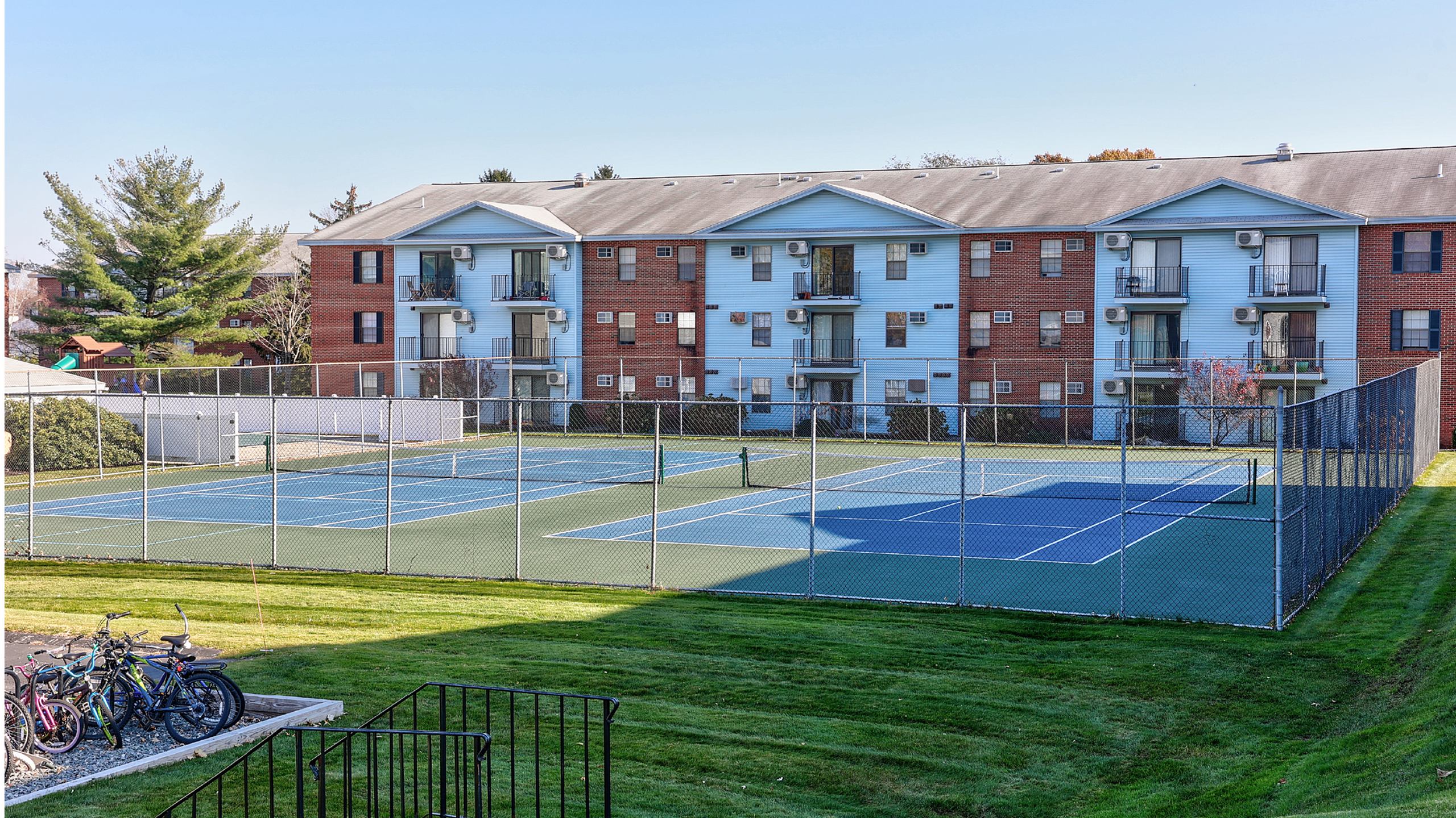 Charming apartment complex with vibrant tennis courts, lush green surroundings, and inviting balconies for a perfect leisure lifestyle.