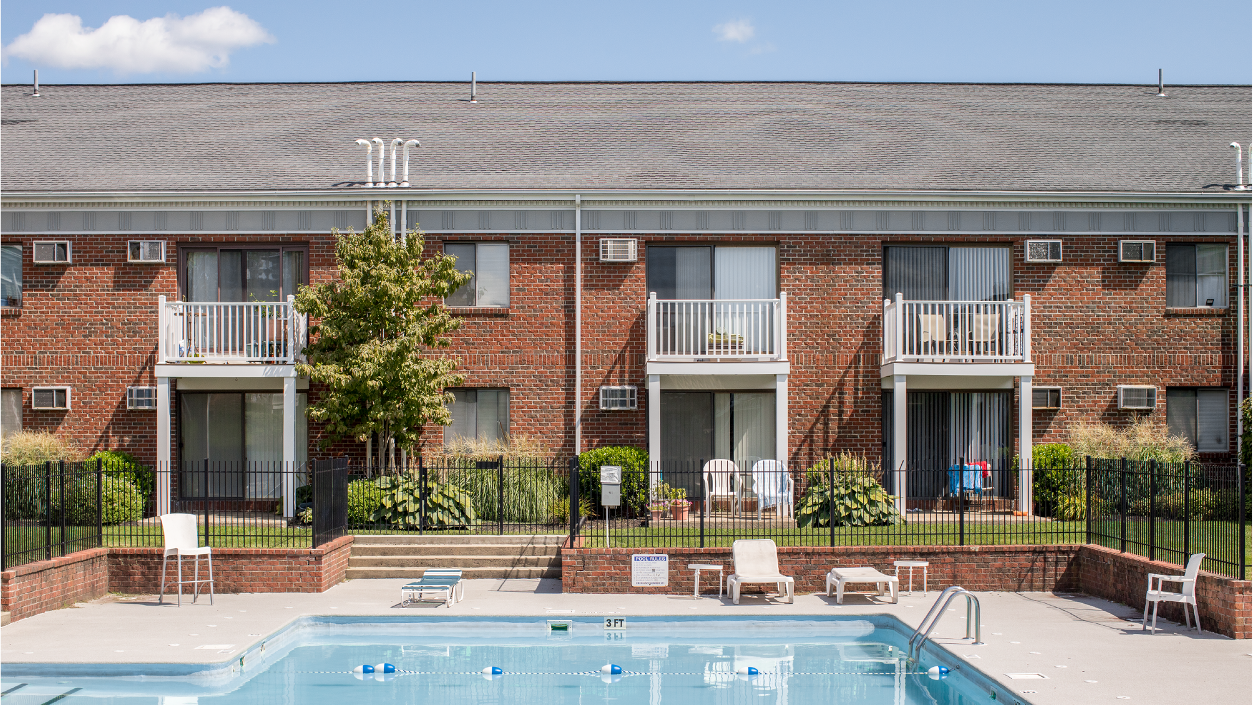 Charming apartment complex showcasing sunlit balconies and a sparkling pool, surrounded by lush greenery for relaxed living.