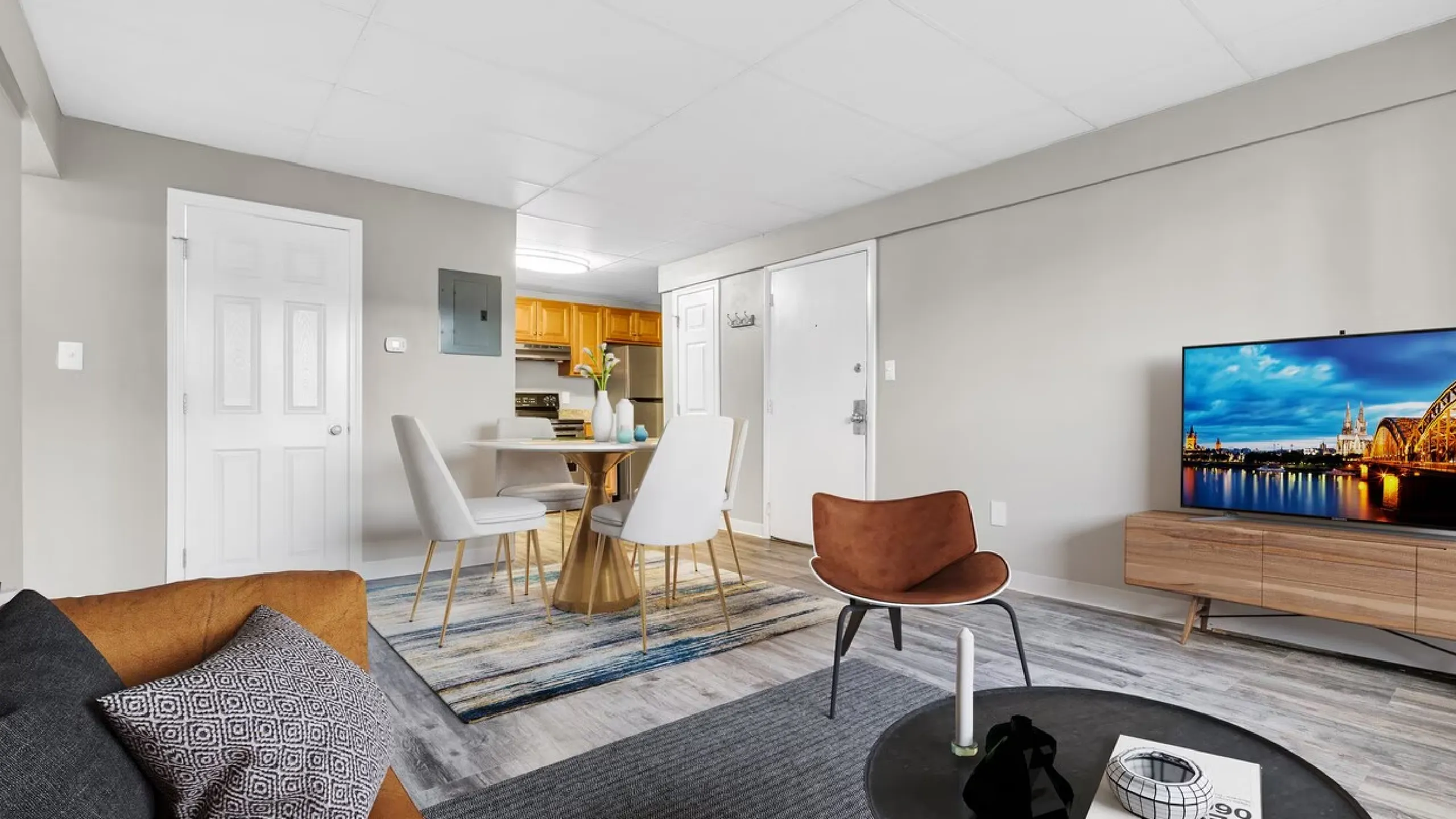 Modern living room with stylish furniture, flat-screen TV, and open-layout view into a cozy dining area and kitchen. Warm tones and contemporary decor create an inviting home atmosphere.