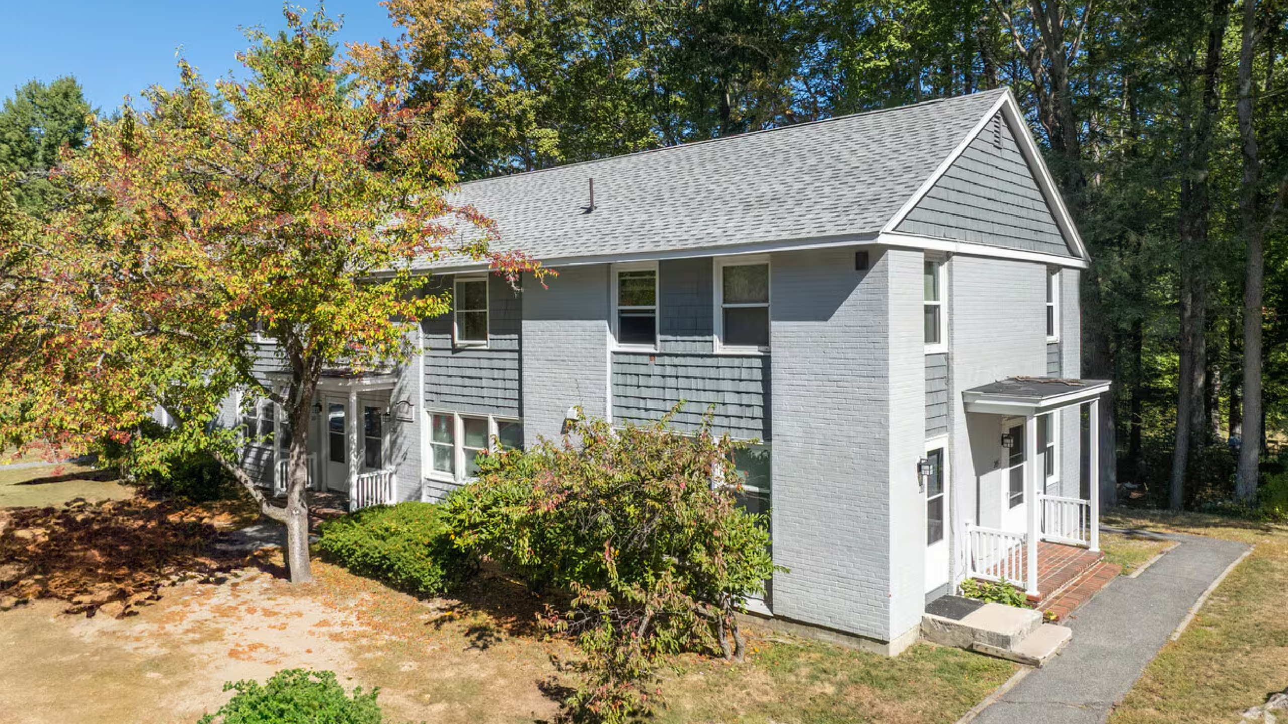 Charming split-level home set amidst lush greenery, showcasing a classic gray exterior with bright white trim, nestled in a serene suburban neighborhood.