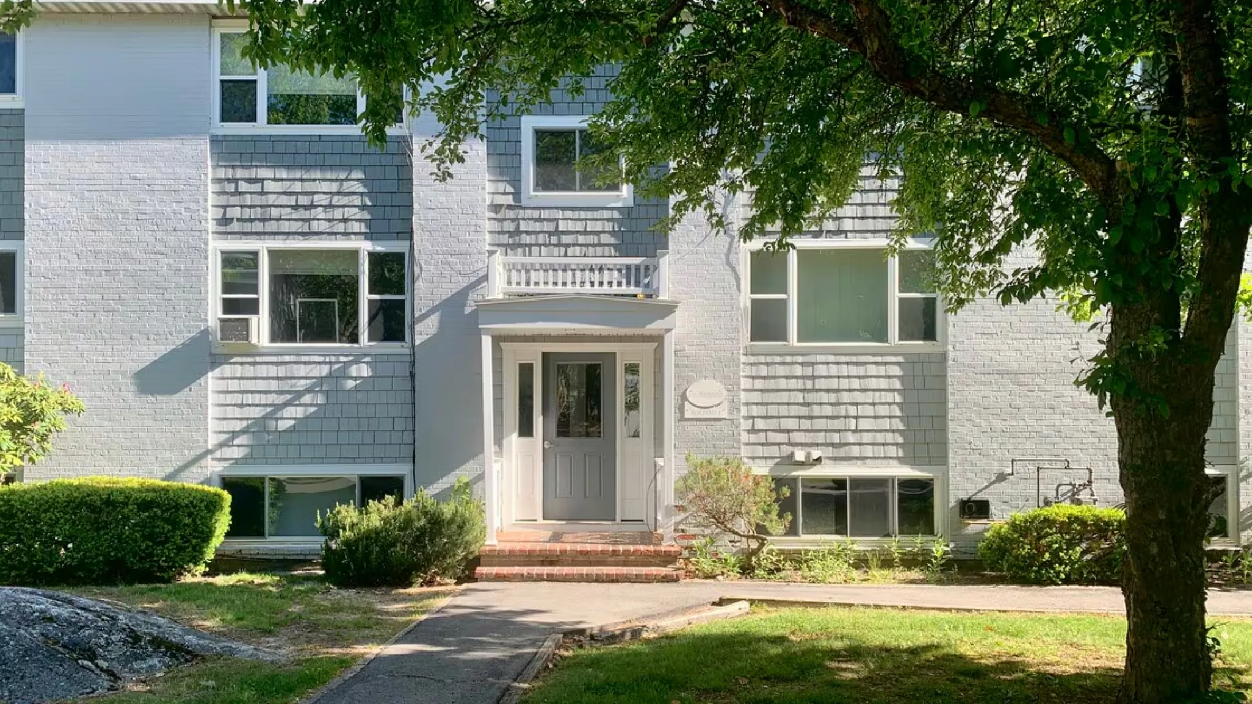 Charming suburban apartment building with welcoming entrance surrounded by lush greenery and serene trees.