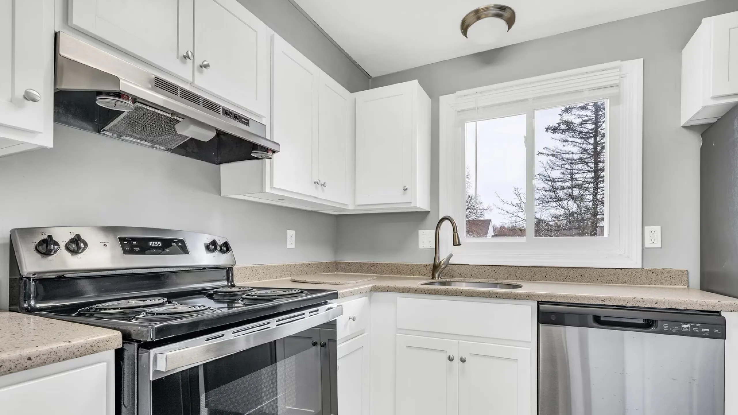 Modern kitchen with sleek stainless steel appliances, elegant white cabinets, and a bright window view.