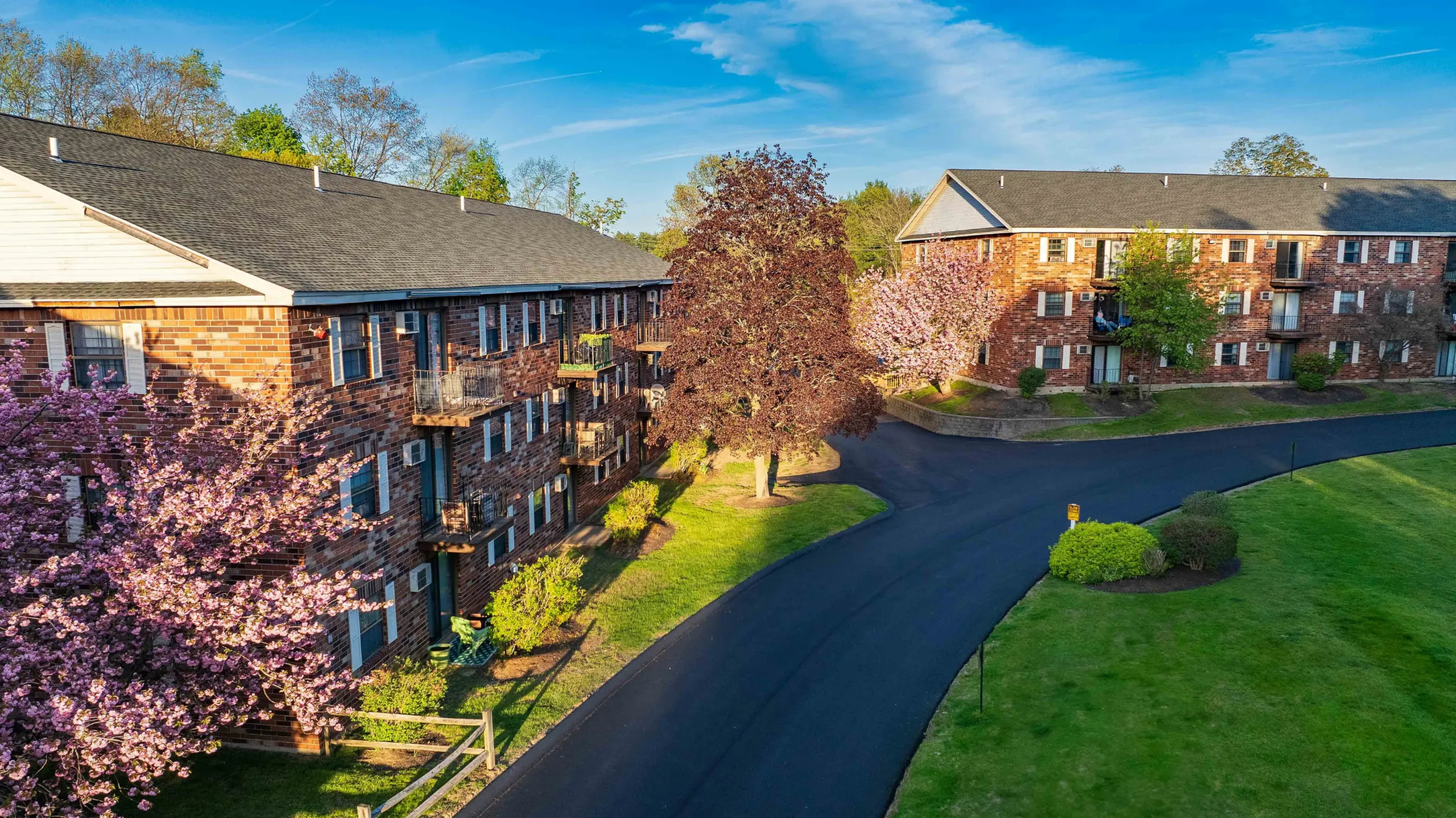 Charming brick apartment complex surrounded by lush greenery and blooming trees, featuring scenic views and a welcoming atmosphere.