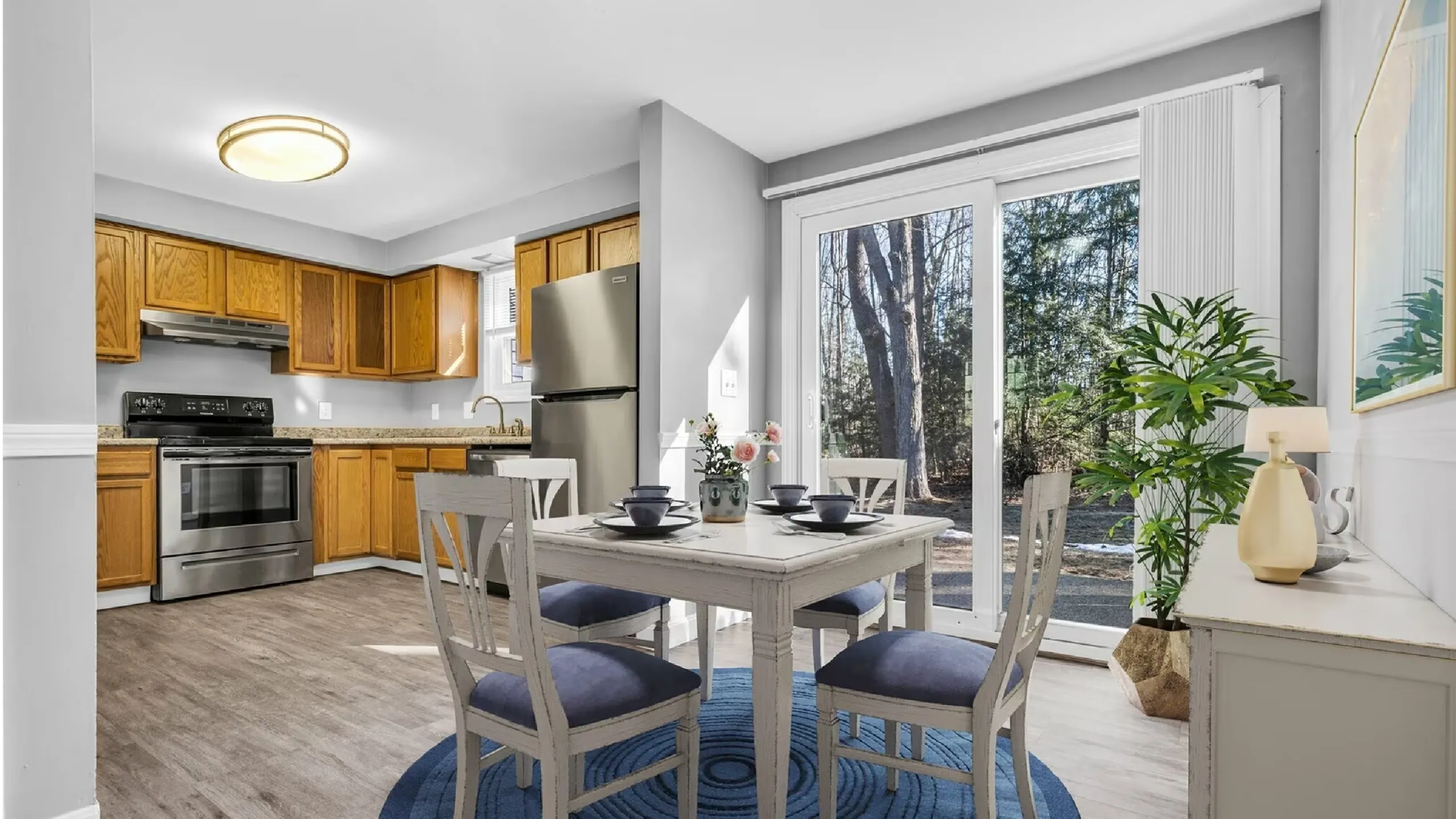 Bright and inviting kitchen-dining area with wooden cabinetry, stainless steel appliances, and large glass doors opening to a scenic outdoor view.