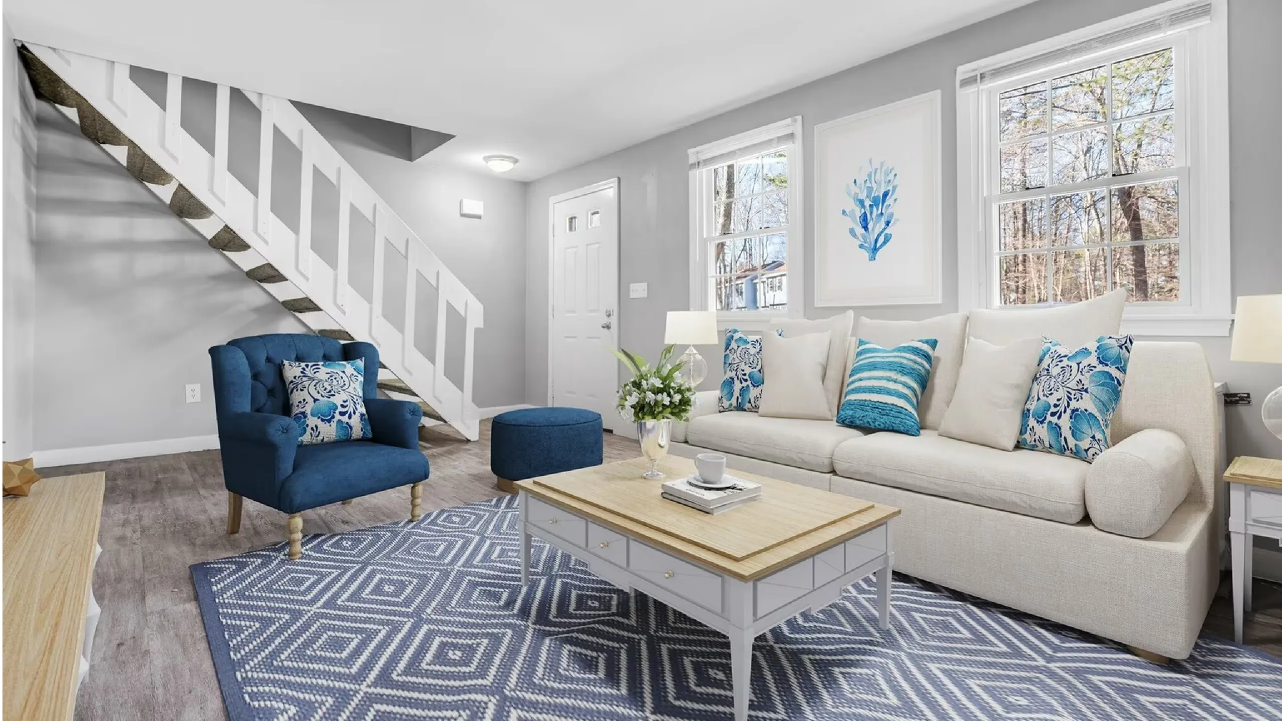 Chic living room with stylish blue accents, a cozy beige sofa, and elegant modern decor under a staircase.