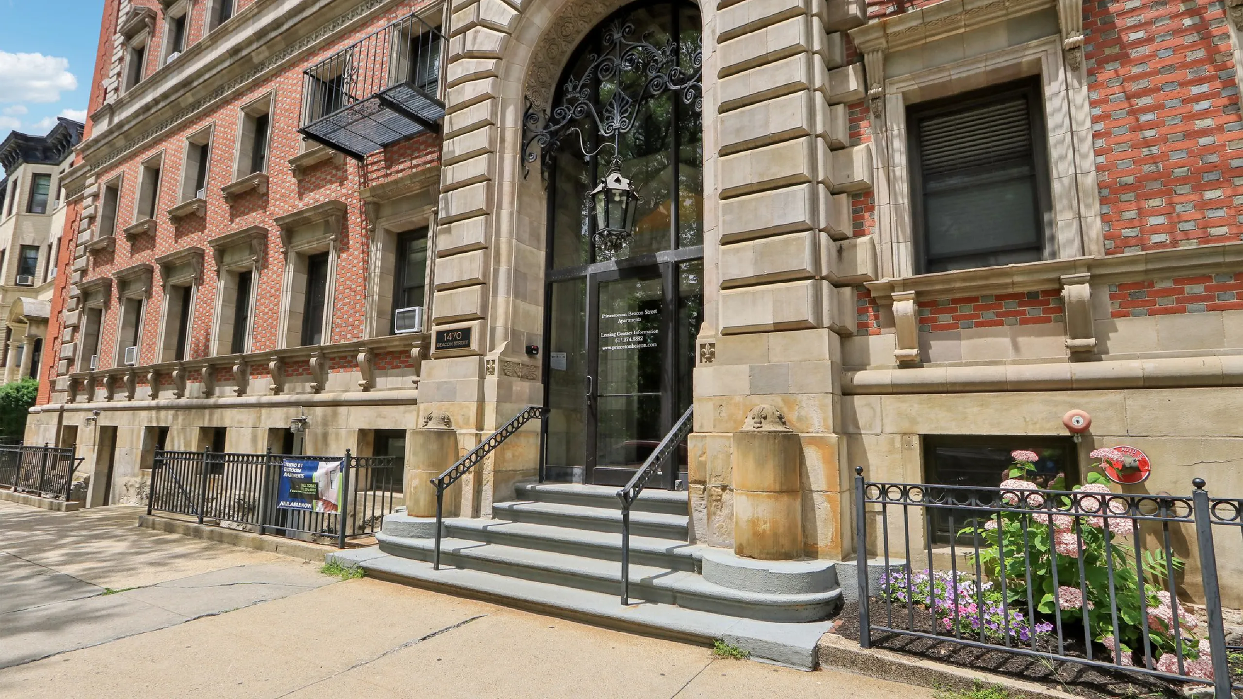 Elegant red-brick apartment building with ornate entrance, surrounded by blooming gardens and classic architectural details, offering refined city living.
