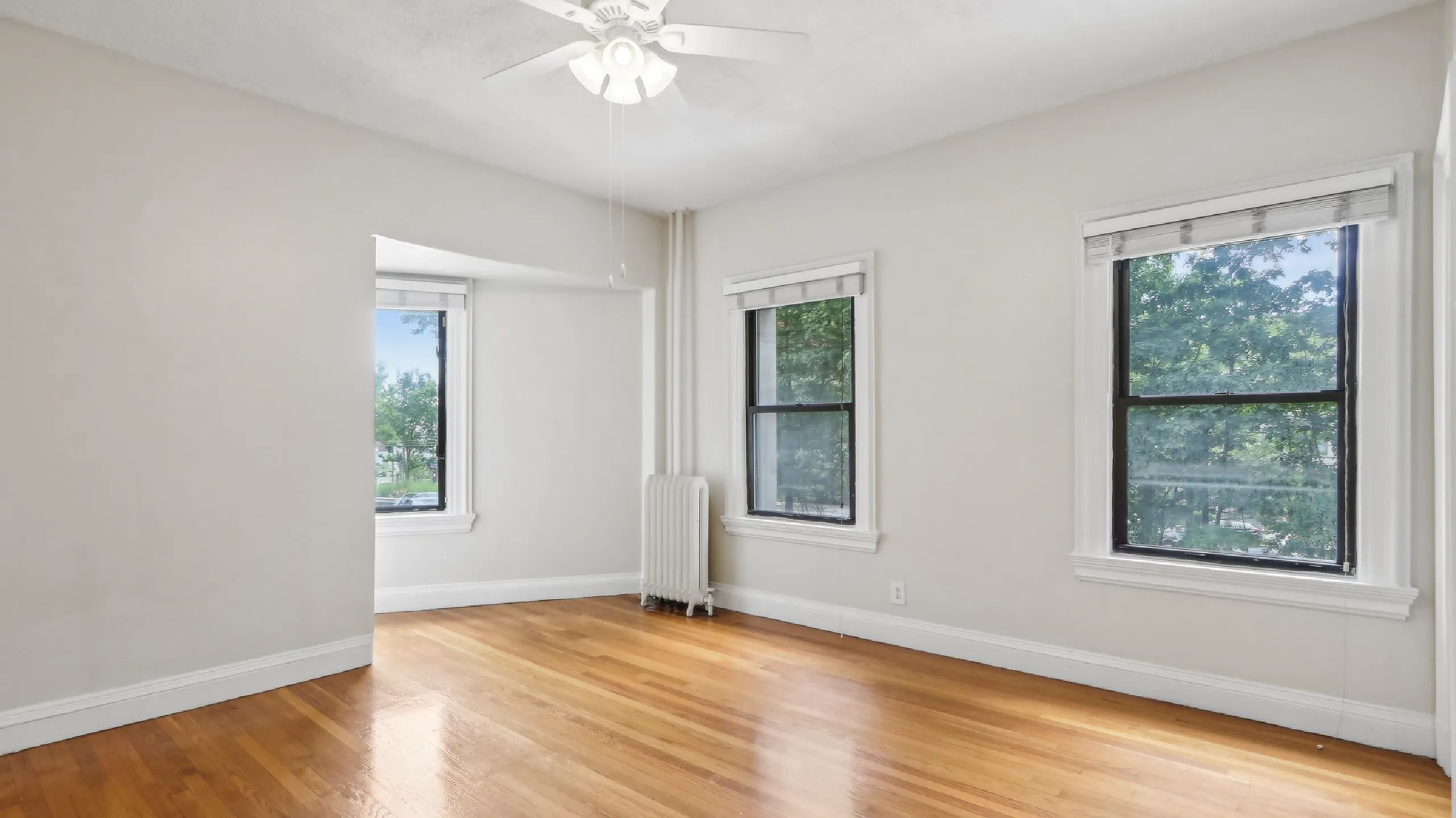 Bright and spacious room with elegant hardwood floors, two large windows offering scenic views, and a ceiling fan for comfort.
