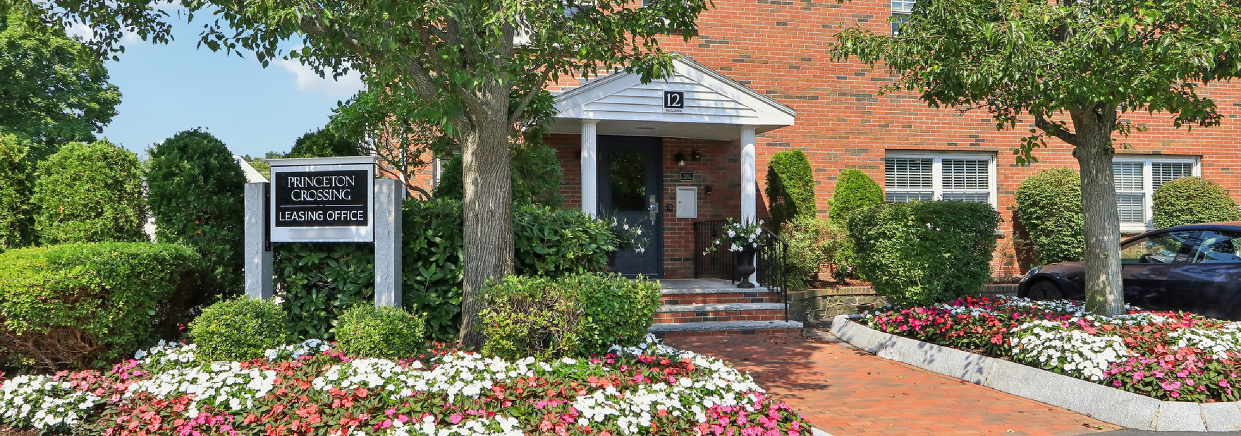 Inviting entrance to Princeton Crossing leasing office surrounded by lush greenery and vibrant flowers, highlighting a friendly and welcoming atmosphere.