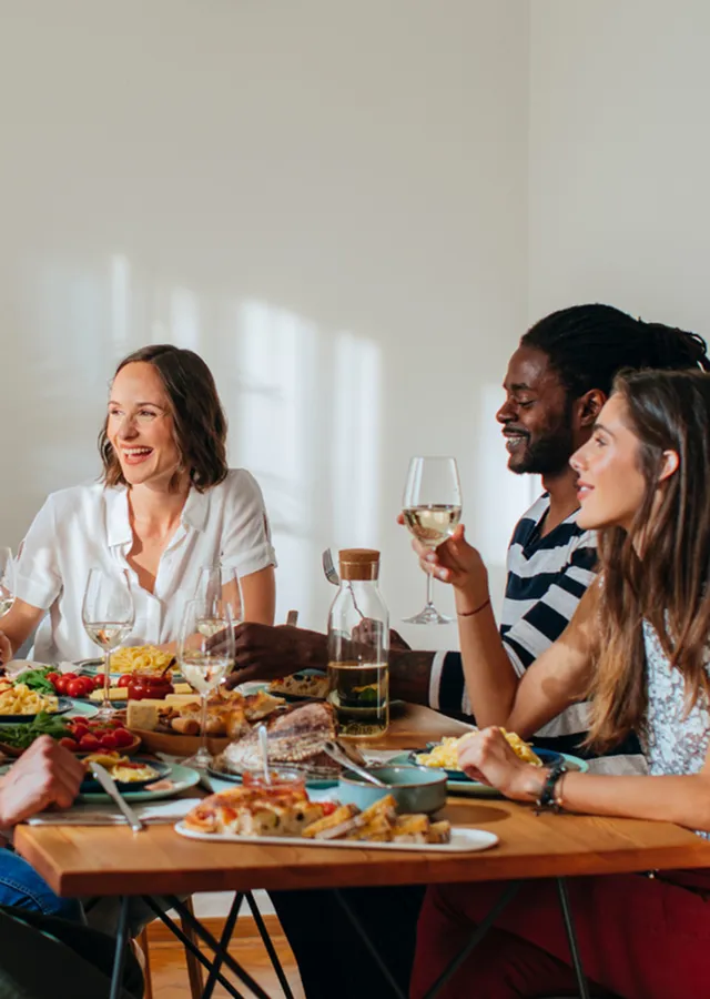Vibrant and joyful dining scene with friends enjoying a delicious meal and wine in a warmly lit, modern apartment.