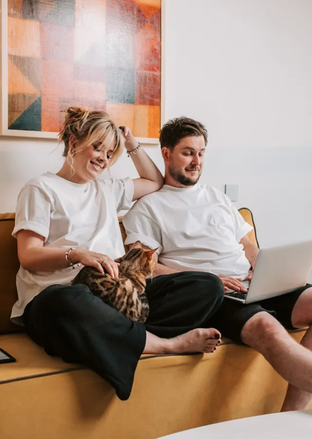 Cozy living room scene with a couple and a cat on a stylish mustard sofa, exuding warmth and comfort.
