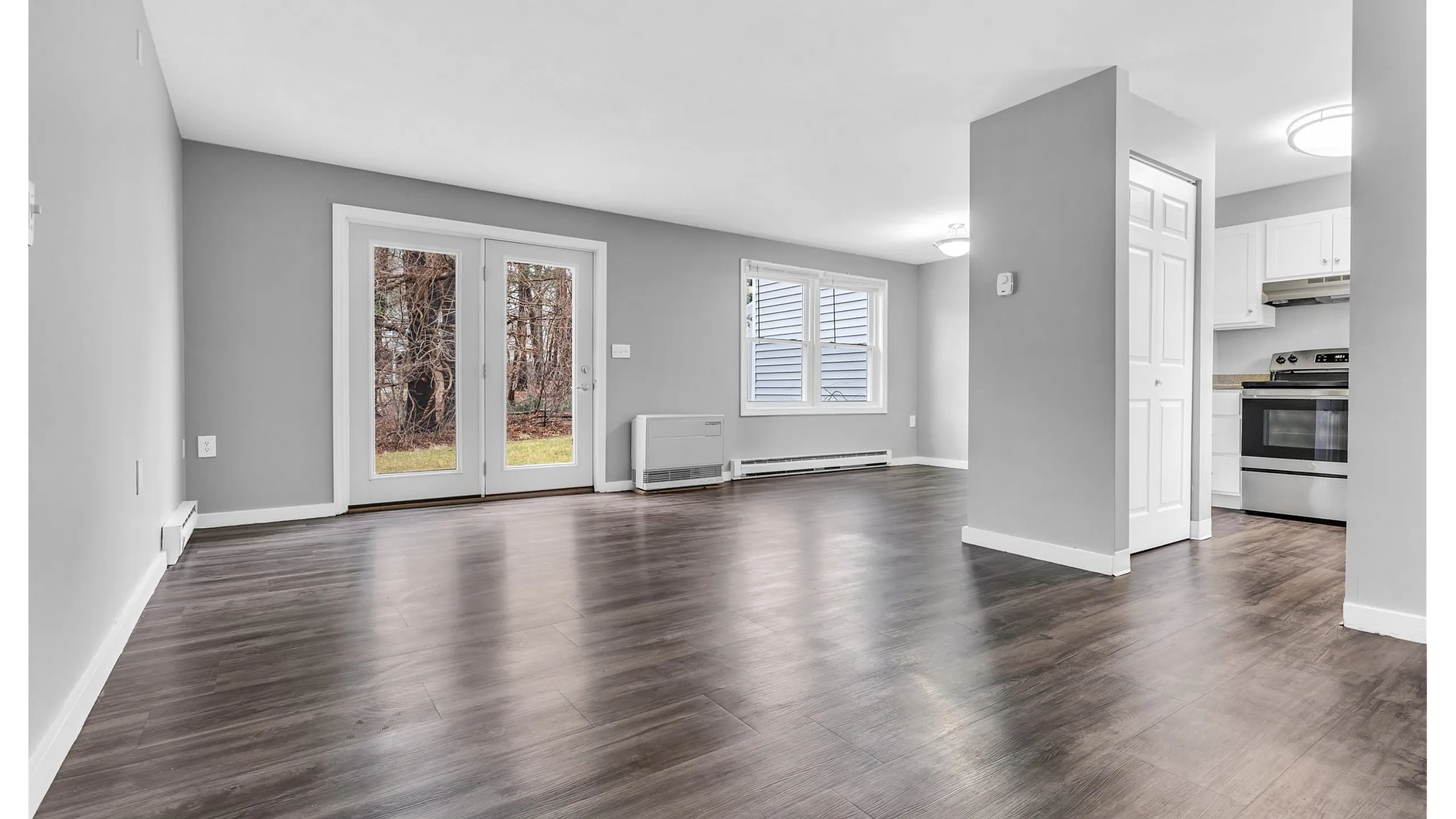 Bright and airy open-concept area featuring elegant hardwood floors, modern kitchen, and large double doors leading to the outdoor area.