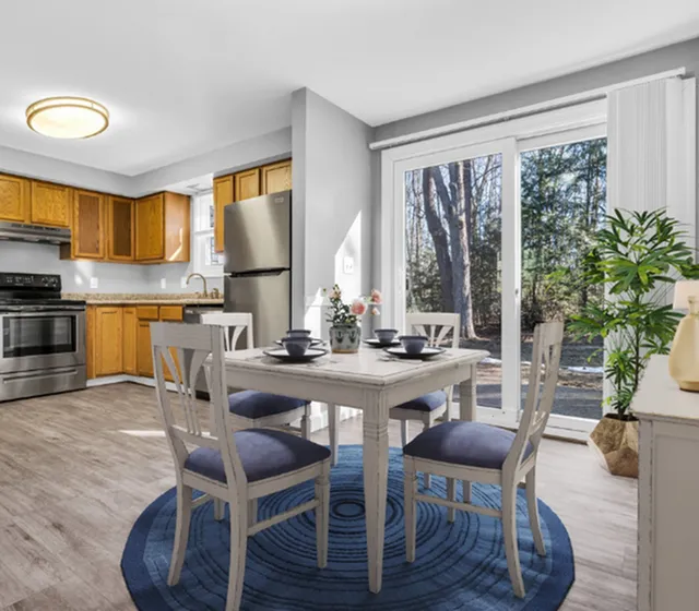 Bright and modern kitchen open to a stylish dining area with elegant furniture, surrounded by natural light and a serene outdoor view.