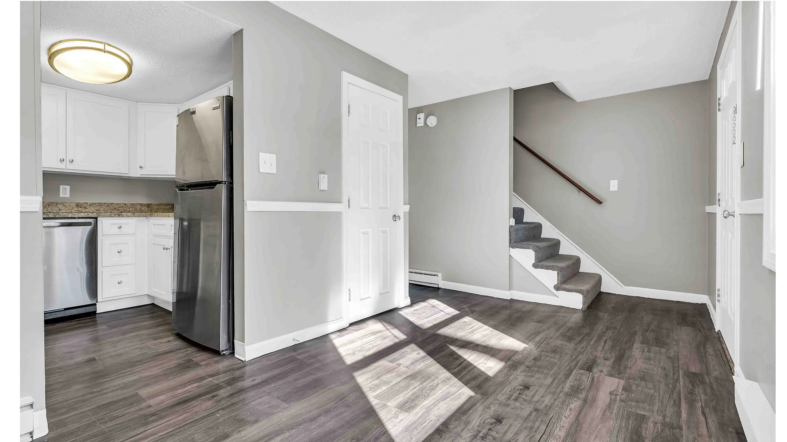 Chic open-concept living area with modern stainless steel kitchen appliances, elegant laminate flooring, and carpeted staircase.