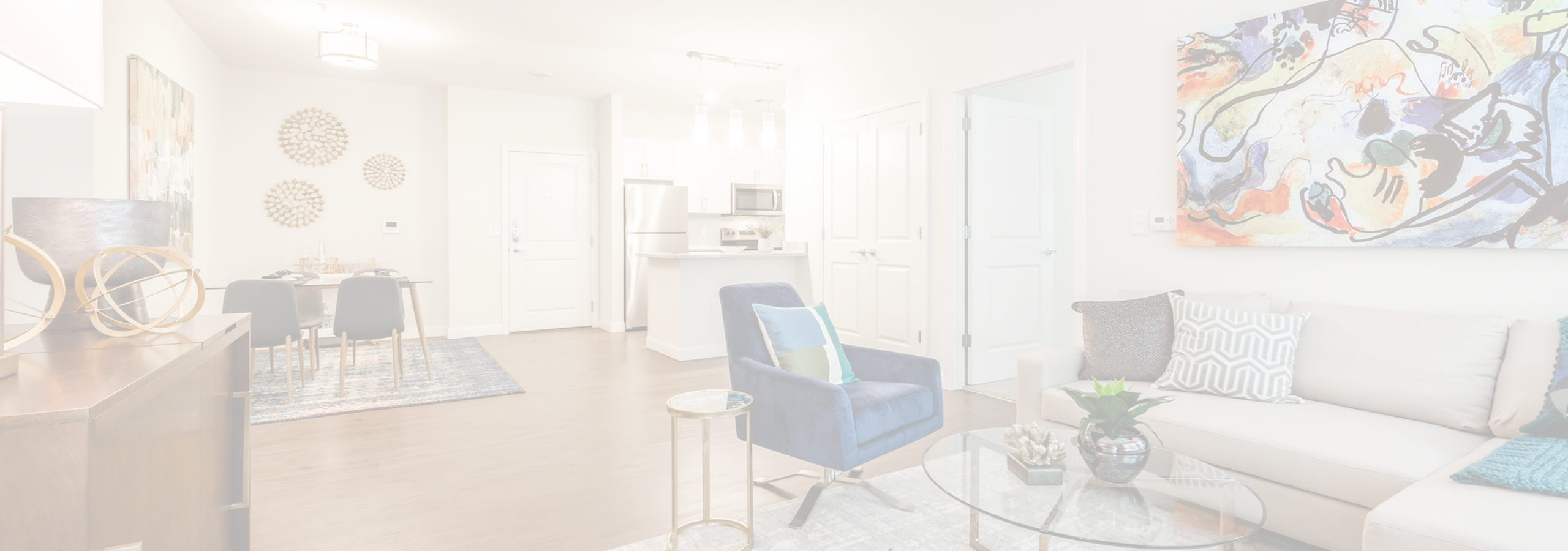 Modern open-concept living room with stylish d&eacute;cor, featuring a vibrant abstract painting, plush seating, and a sleek kitchen in the background.