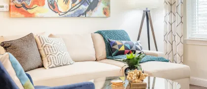 Bright and cozy living room at Mill & 3 Apartments in Chelmsford MA with a comfortable beige sectional sofa, vibrant pillows, sleek floor lamp, and artistic wall art, perfect for creating a welcoming atmosphere.