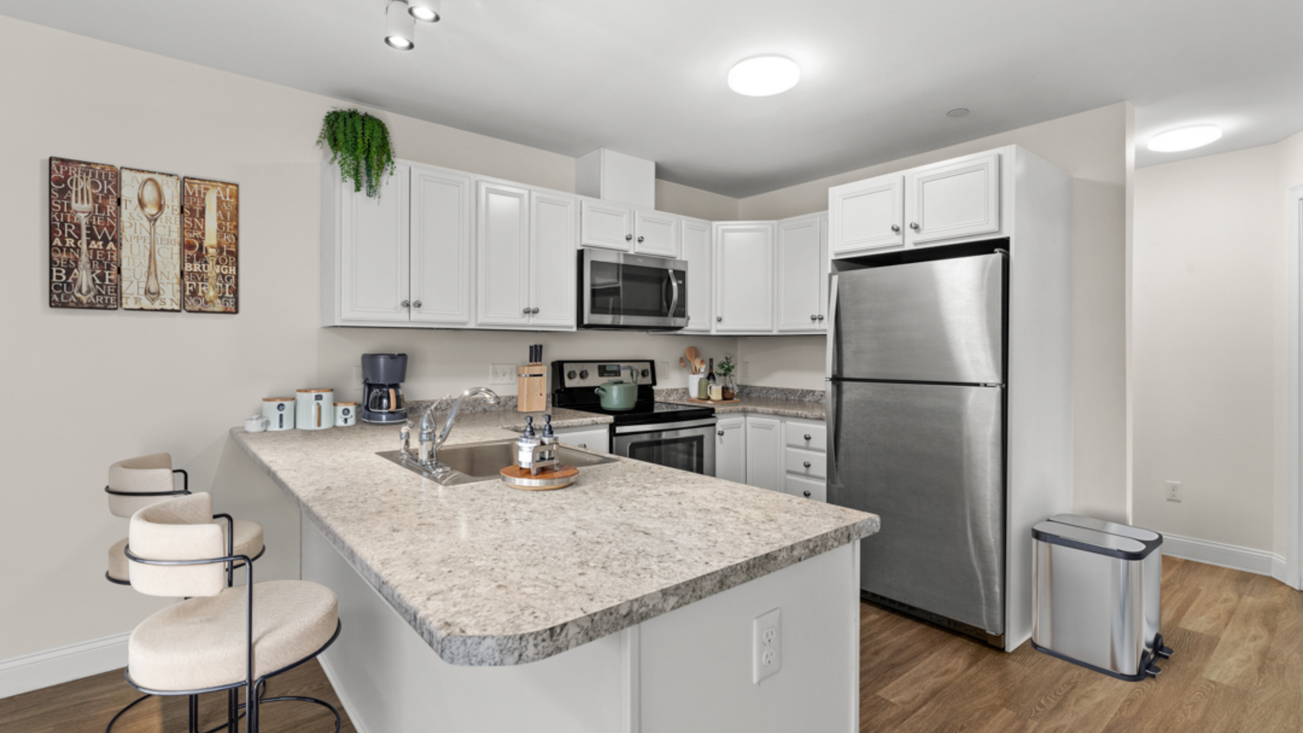 Modern kitchen design featuring sleek stainless steel appliances, elegant white cabinetry, and a spacious granite countertop with stylish bar stools.