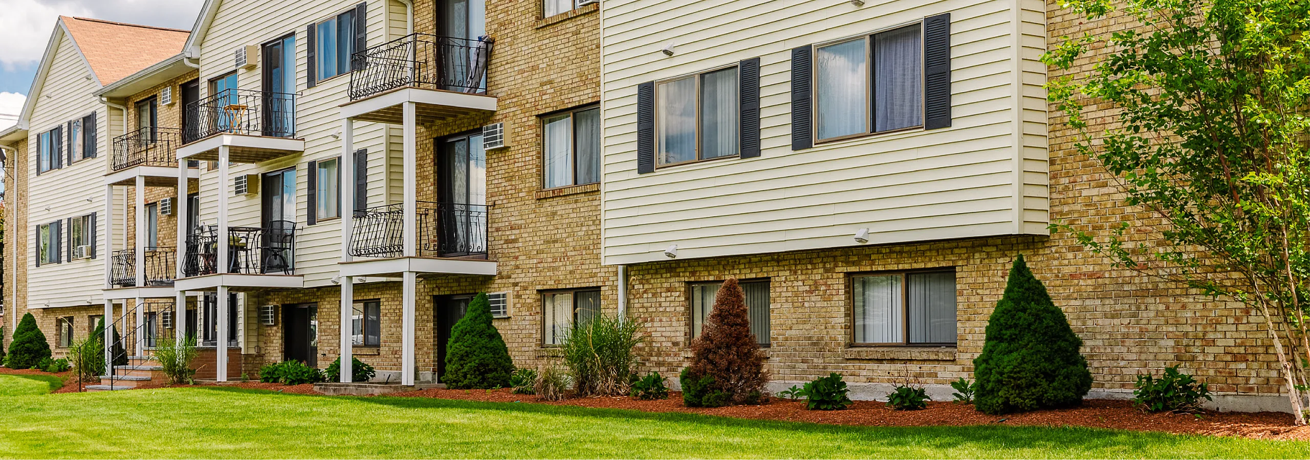 Charming brick apartment building with inviting balconies and lush landscaping, perfect for comfortable living.