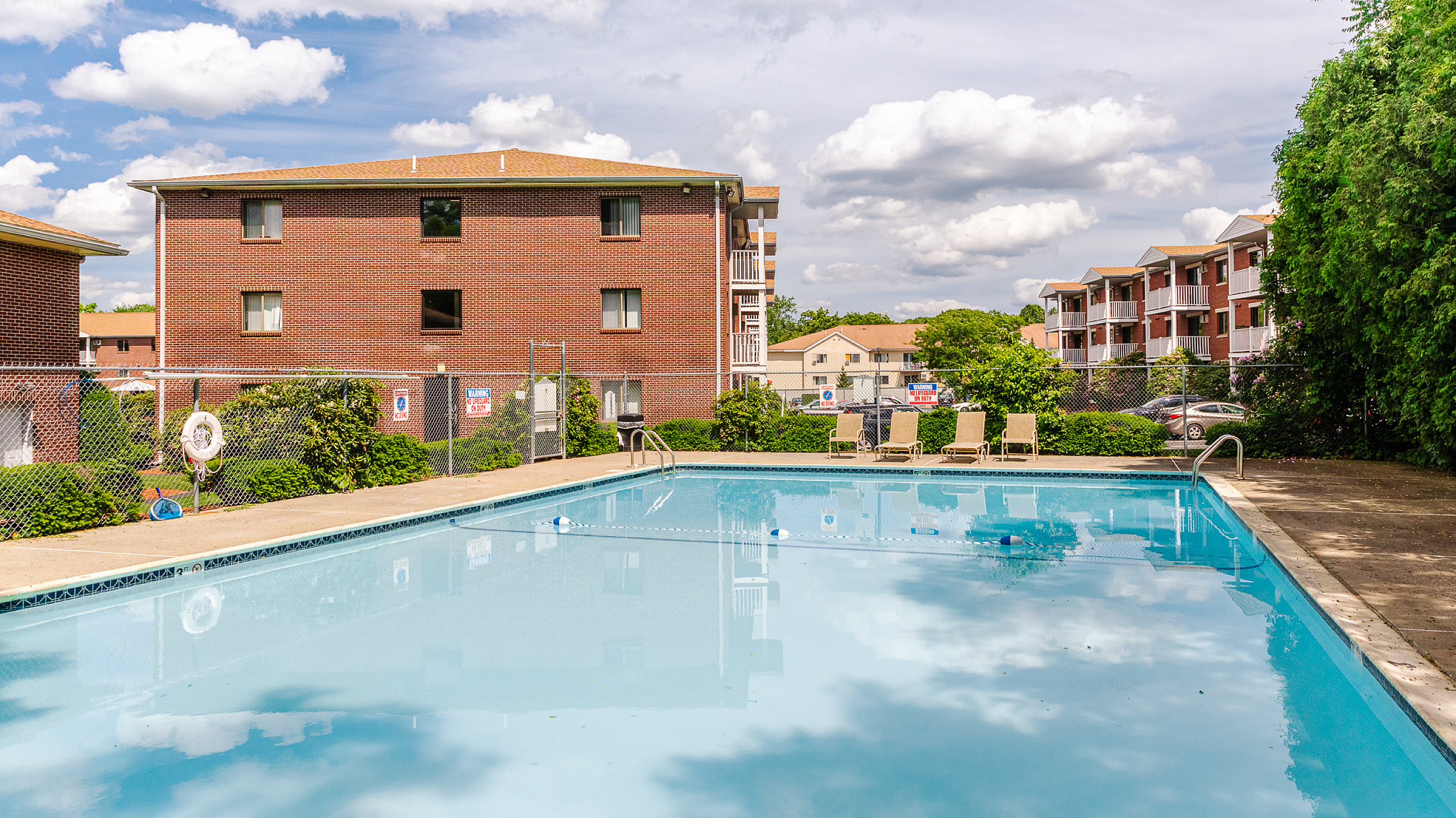 Inviting apartment complex with a sparkling outdoor pool, surrounded by lush greenery and comfortable lounge chairs, perfect for relaxation.