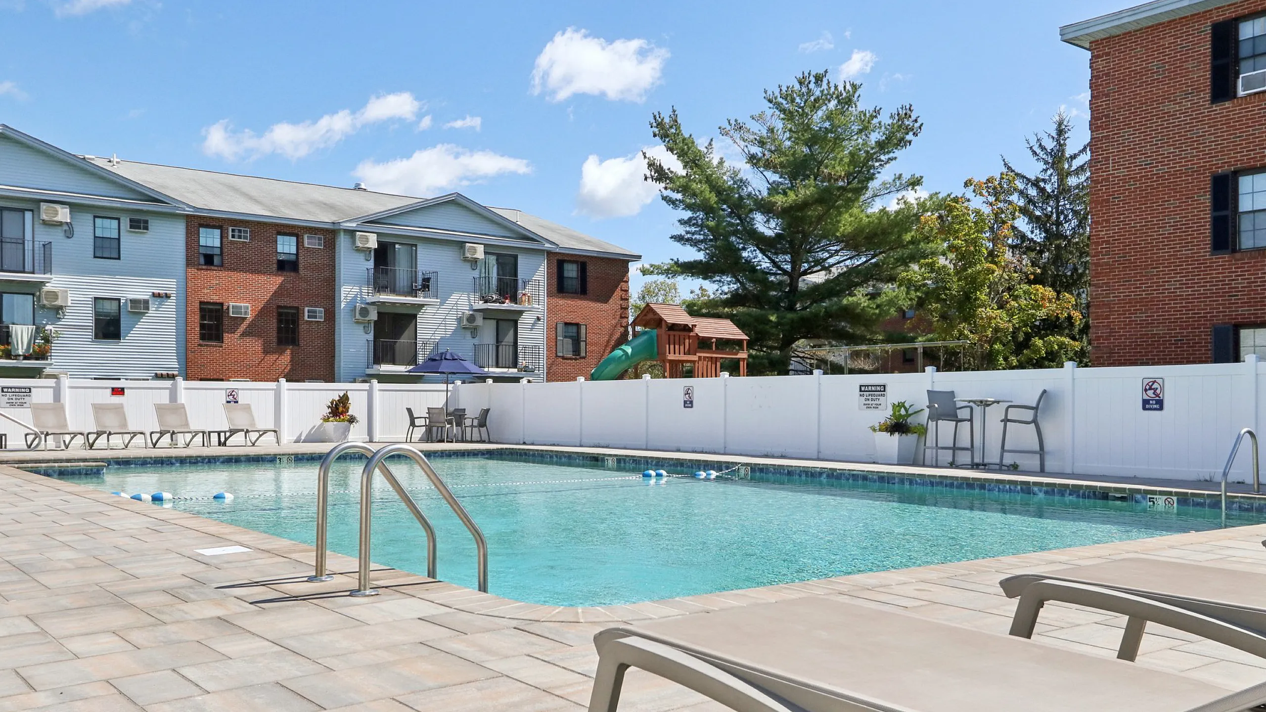Inviting outdoor pool area with comfortable lounge chairs, surrounded by modern apartment buildings and lush trees.