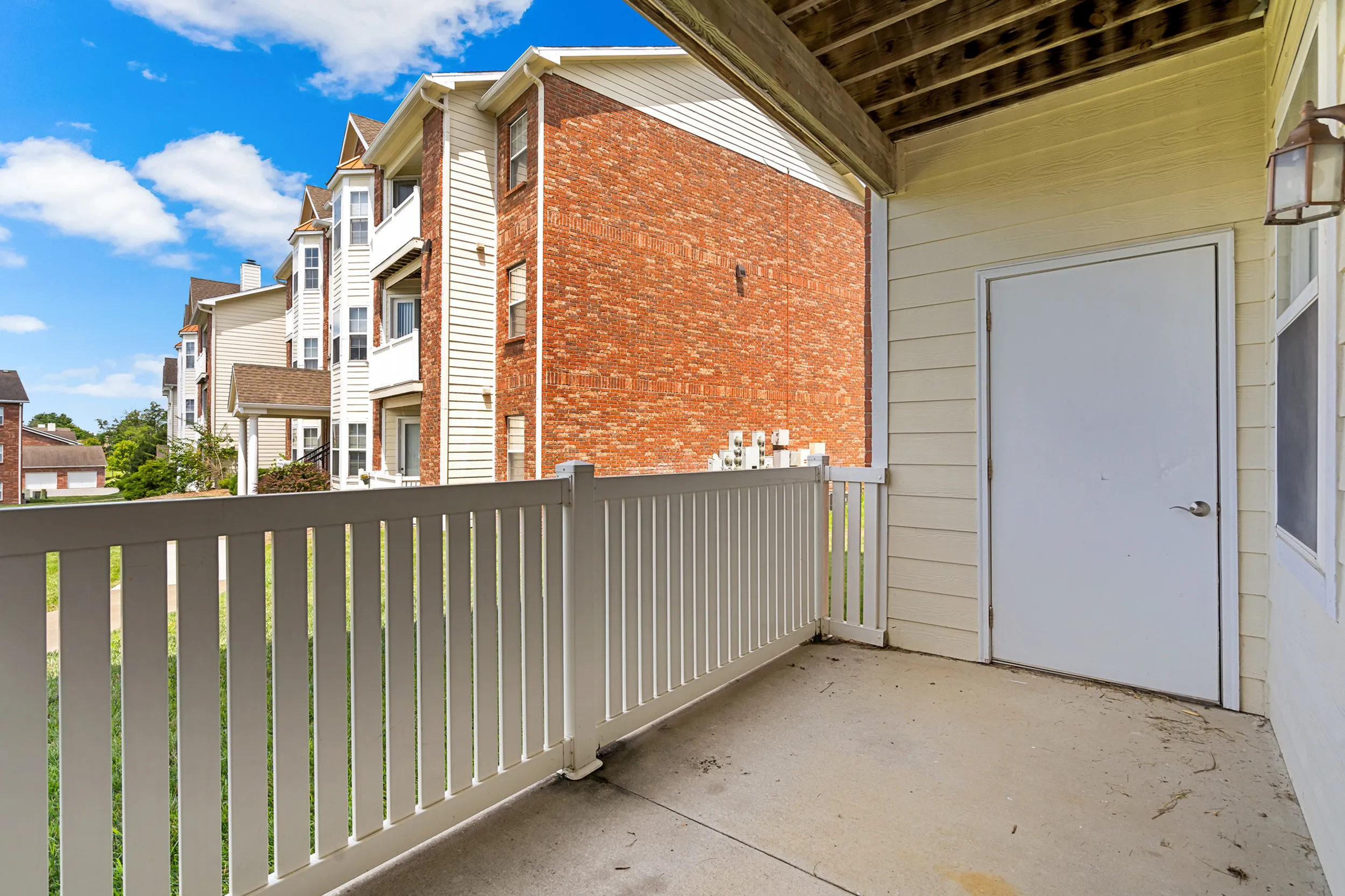 Charming apartment balcony with a white railing, offering picturesque views of a sunny residential neighborhood with brick buildings.