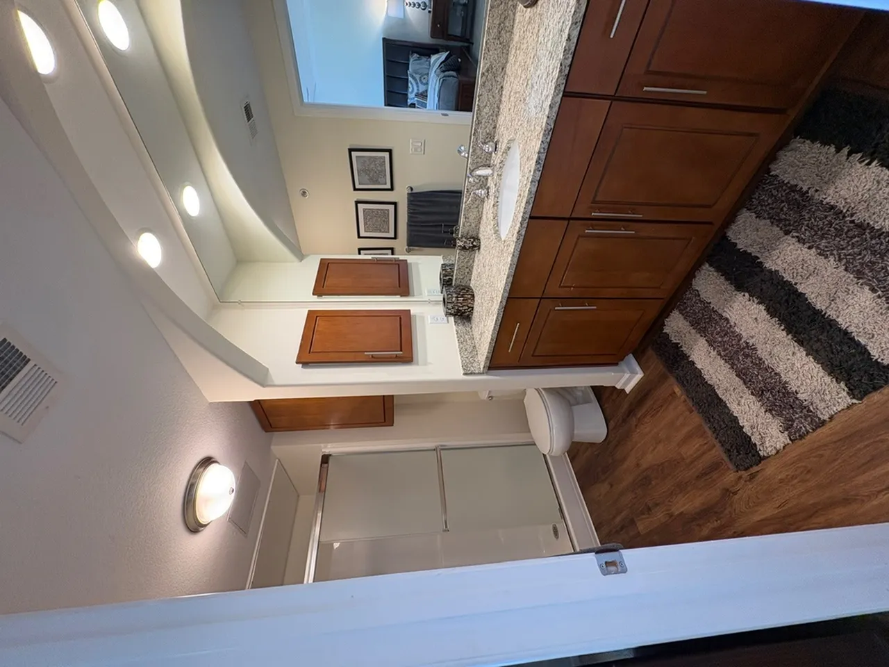 Elegant bathroom with granite countertop, wooden cabinetry, and cozy striped rug, adjacent to a bright, inviting bedroom.
