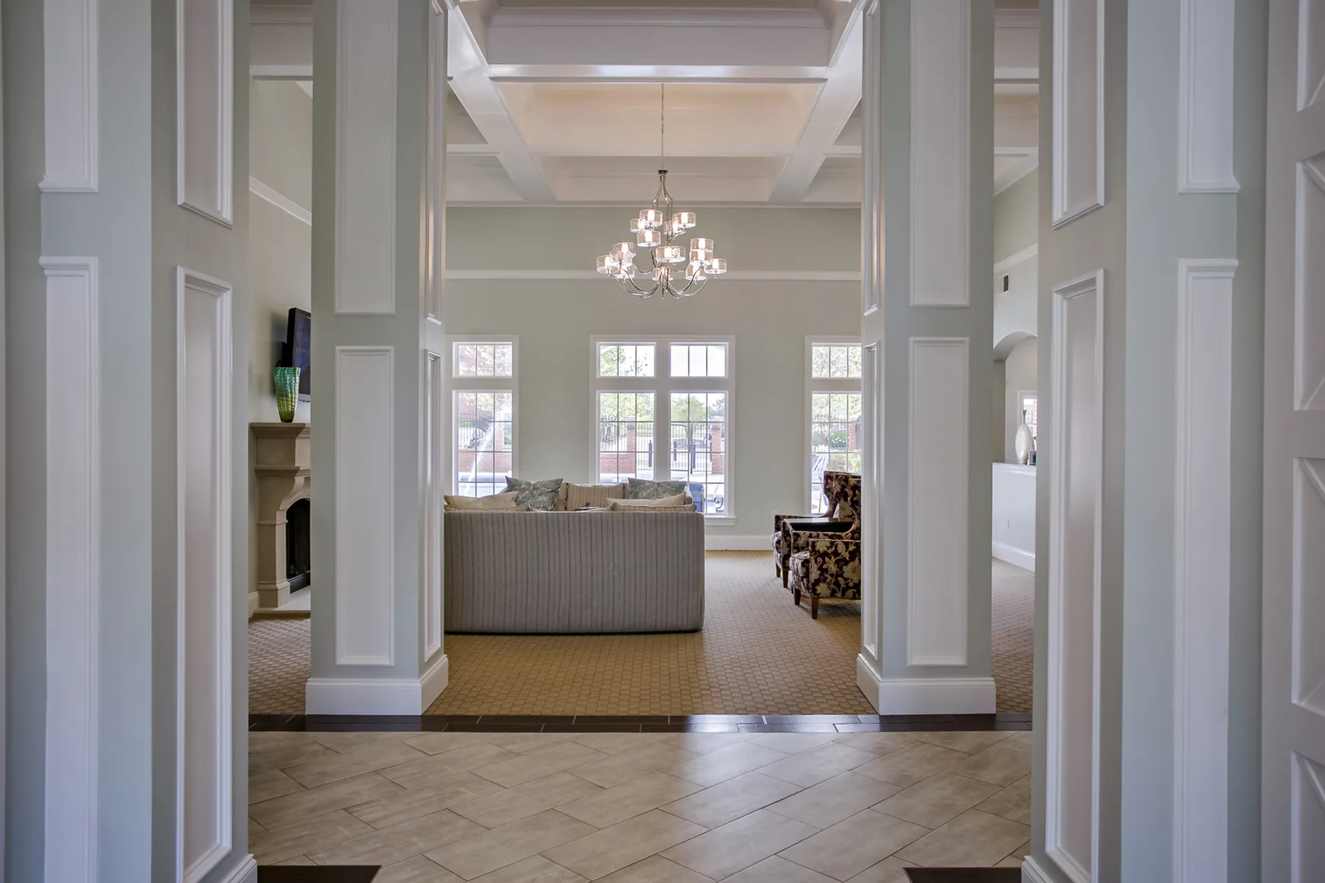 Elegant living room with high ceilings, polished floors, and a stylish chandelier, inviting natural light through large windows.