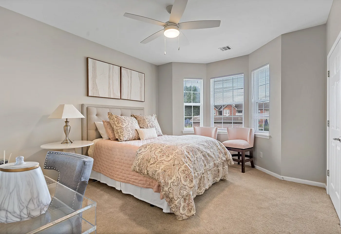 Charming bedroom with elegant decor, featuring a cozy bed, stylish accent chairs, and a sunlit bay window.