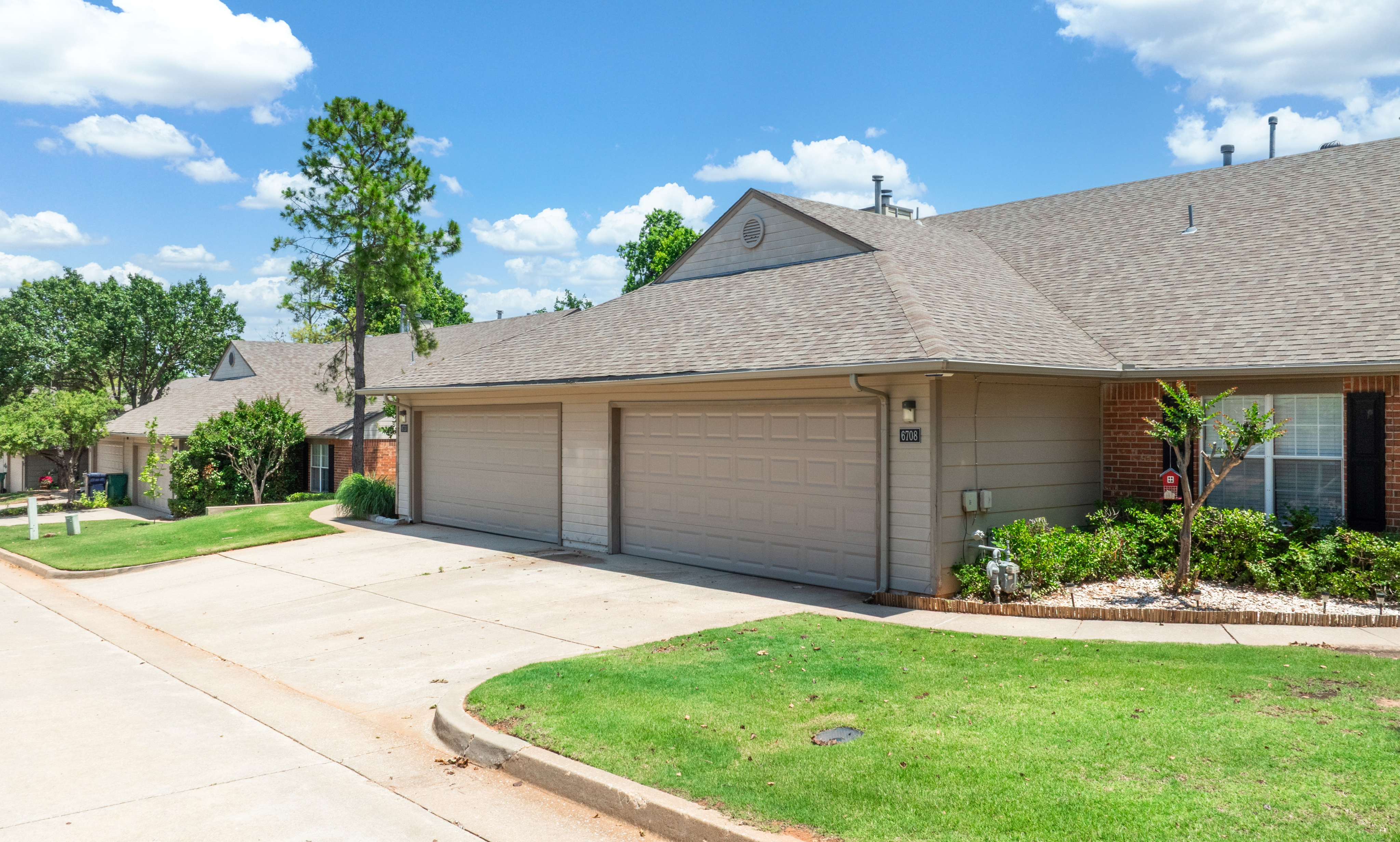 Charming suburban home with a spacious two-car garage, lush greenery, and bright blue skies, ideal for family living.